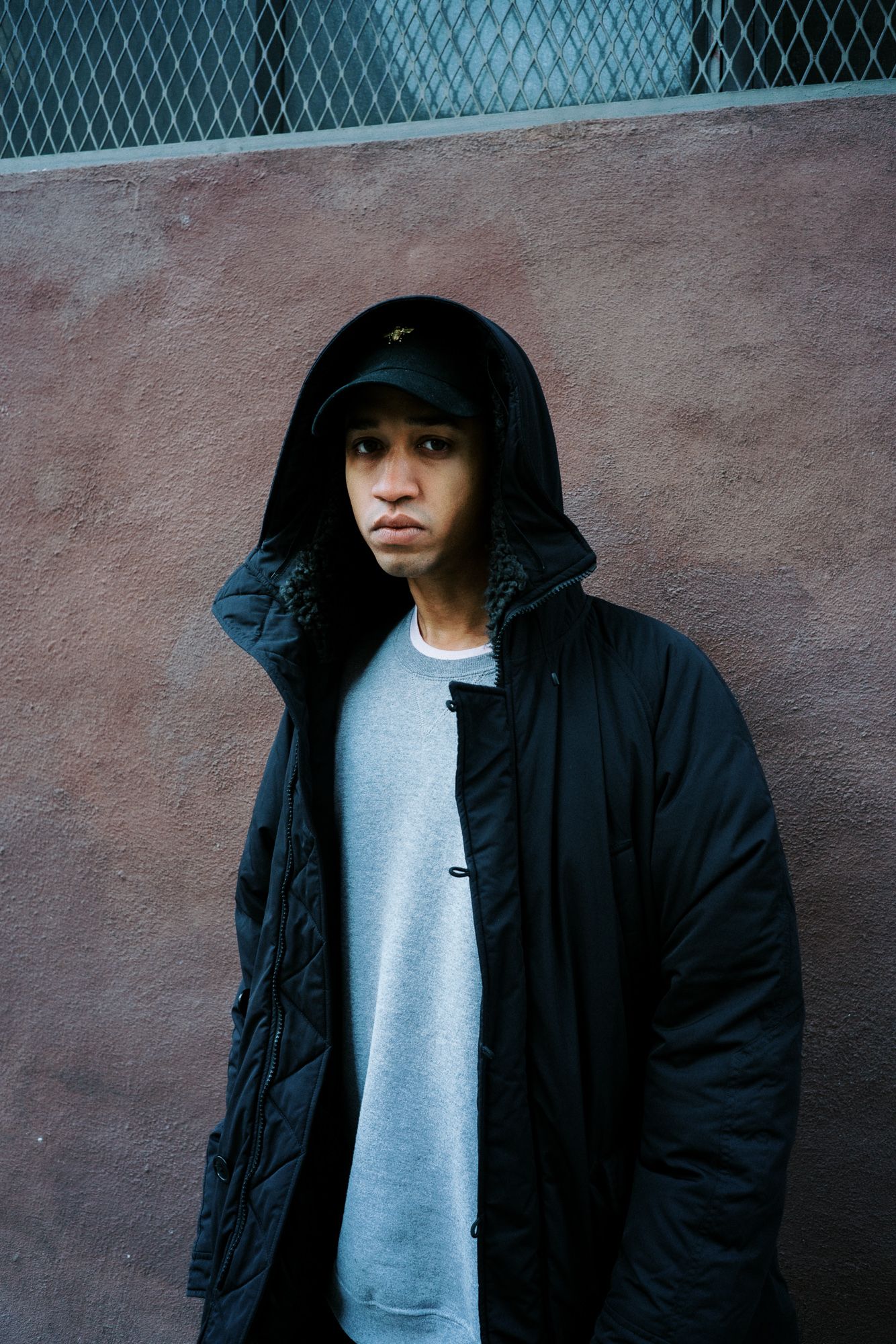 Urban portrait series showing person in black hoodie against textured wall.