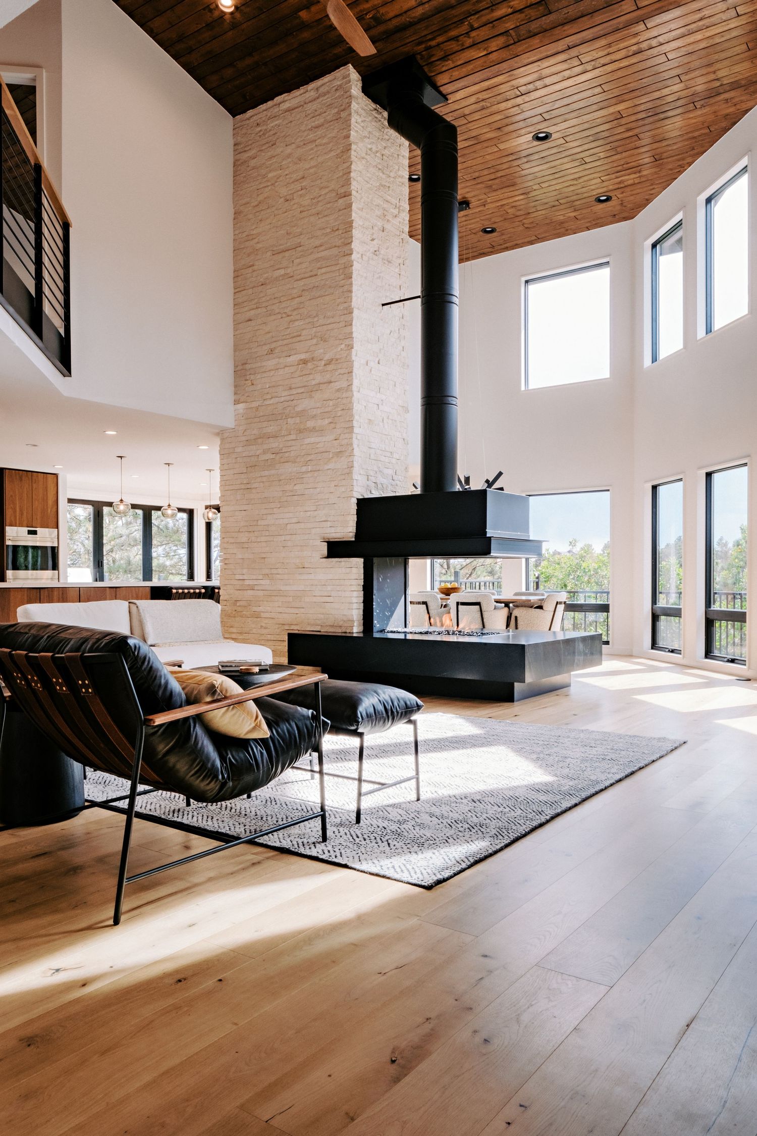 Spacious living area with vaulted wooden ceiling, stone walls, and floor-to-ceiling windows.