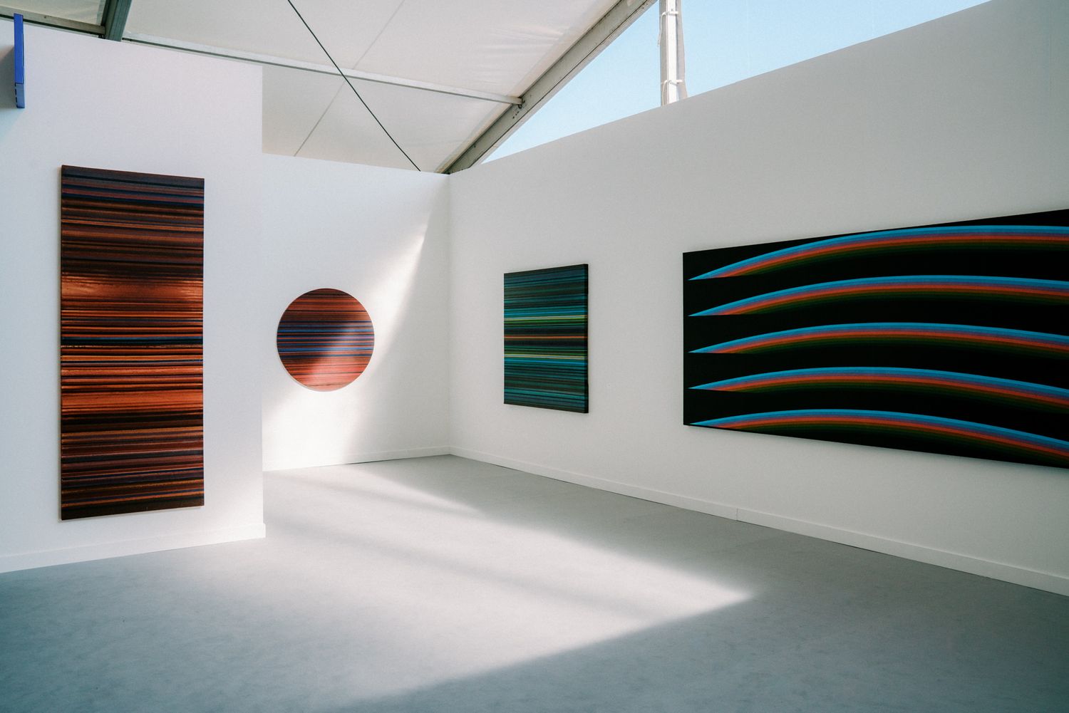 Modern art gallery with abstract striped paintings in red, green, and blue tones displayed on white walls.