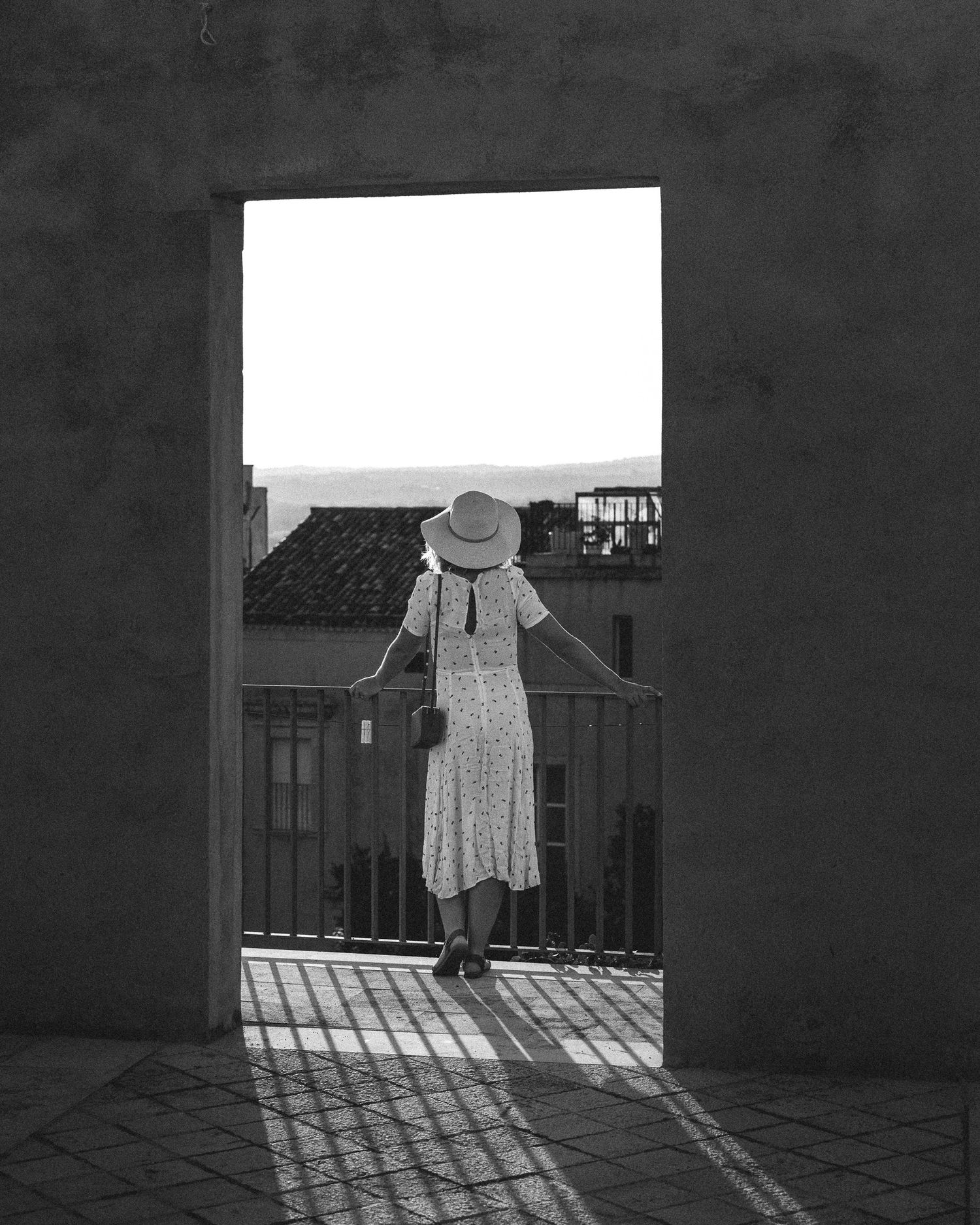 A dress hanging on a clothesline casts dramatic shadows on a white wall in black and white photography.