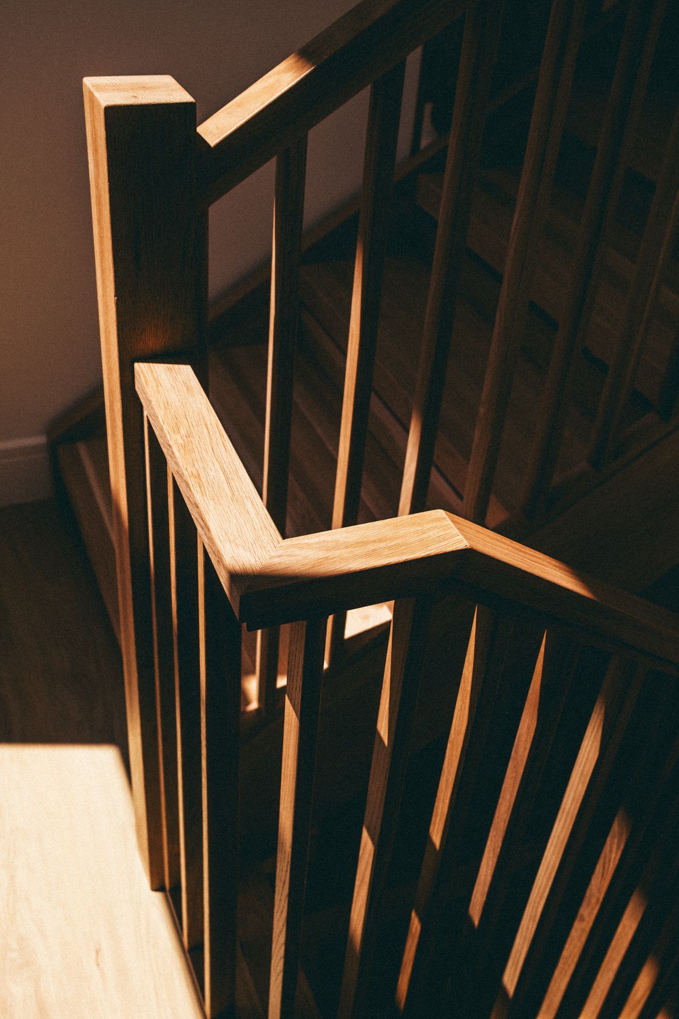 Elegant dark wood staircase railing with vertical spindles and angled handrail, illuminated by warm natural light.