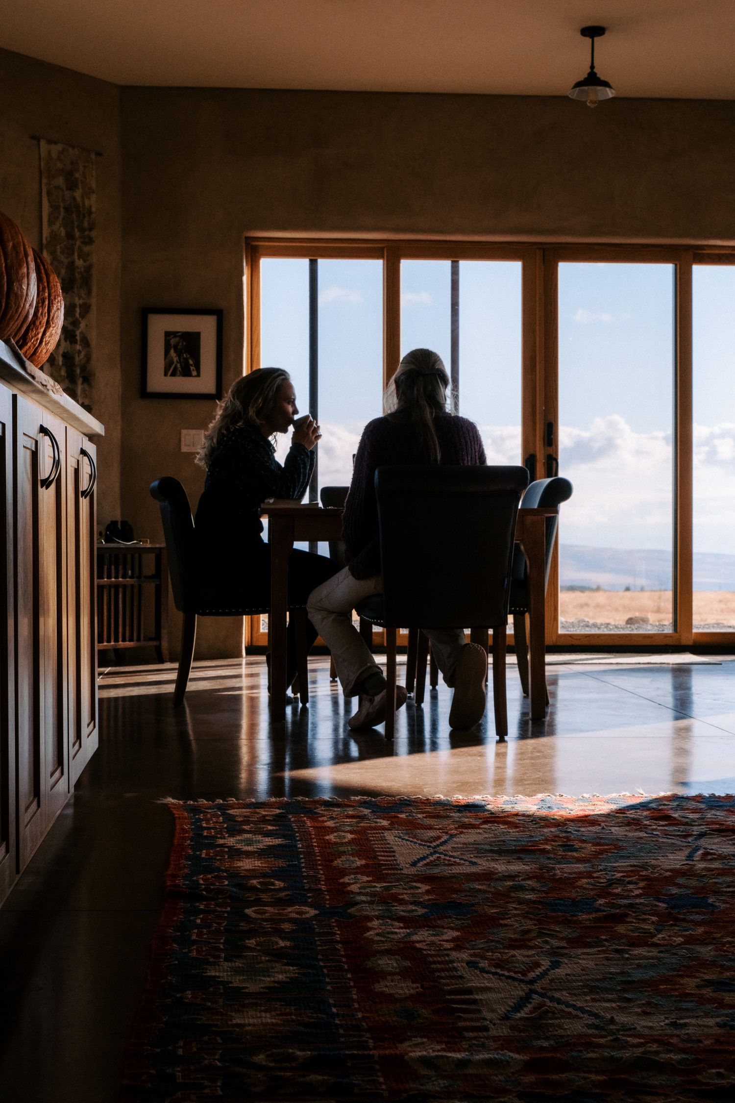 Silhouetted figures seated at a dining table against large windows with mountain views.