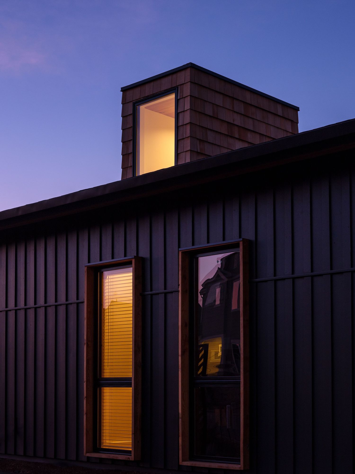 Modern building exterior with illuminated windows against a twilight sky creating a dramatic silhouette effect.