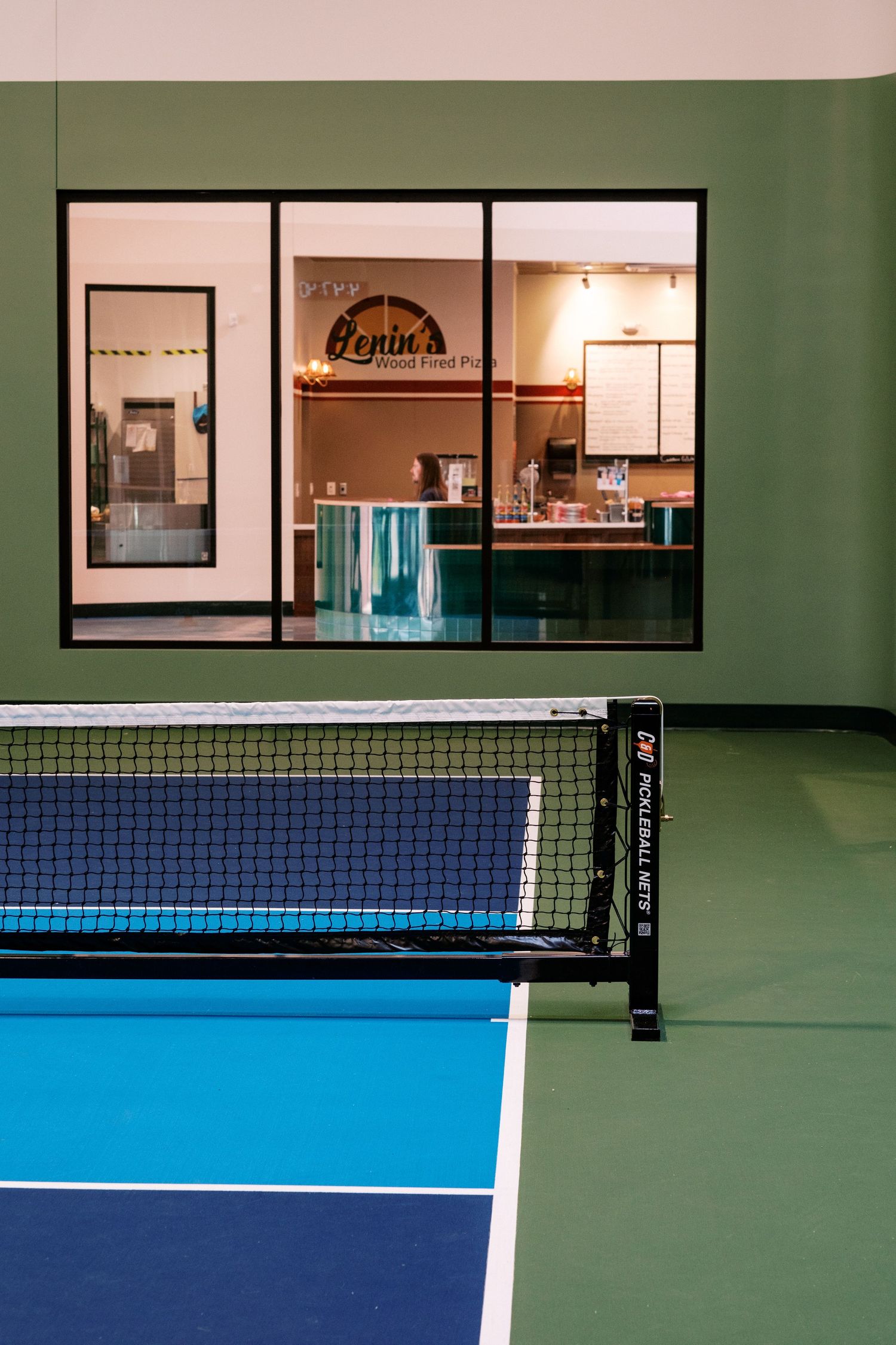 Indoor tennis court with blue and green surfaces separated by a regulation net.