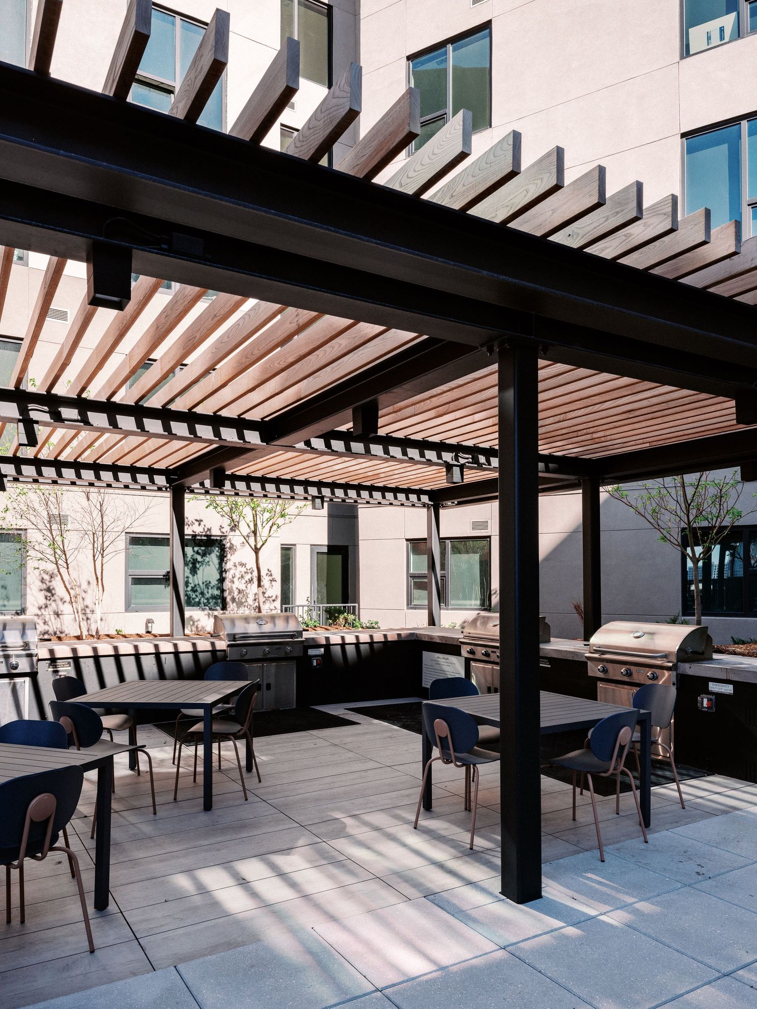 Outdoor dining area with black pergola creating geometric shadows on concrete patio.