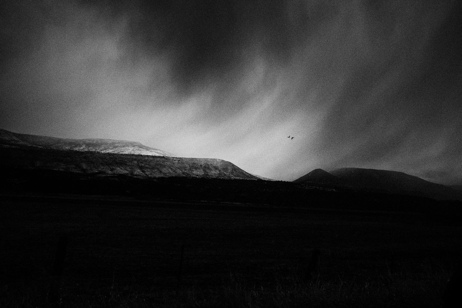 Dramatic stormy sky over mountain silhouettes in black and white.
