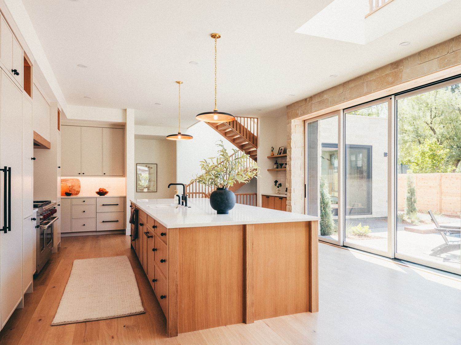 Modern kitchen with wood island, white countertops, pendant lights, and sliding glass doors opening to a patio.