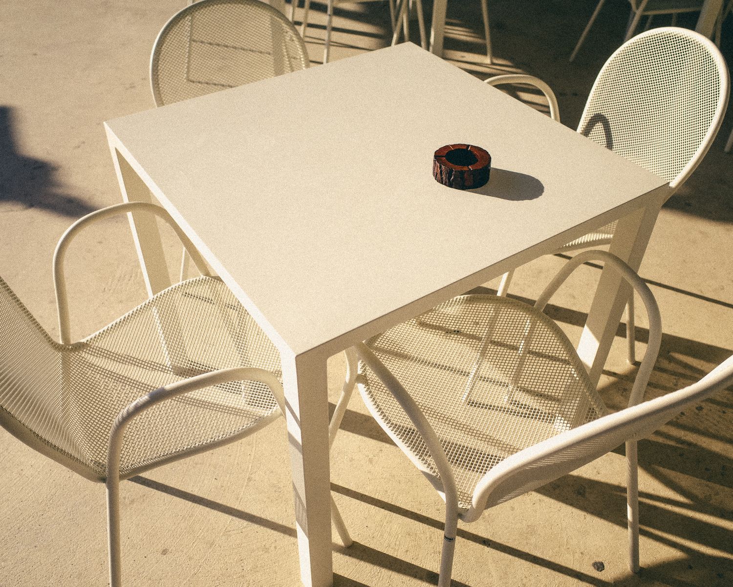 A series of white plastic chairs and tables arranged in a row against a beige wall.