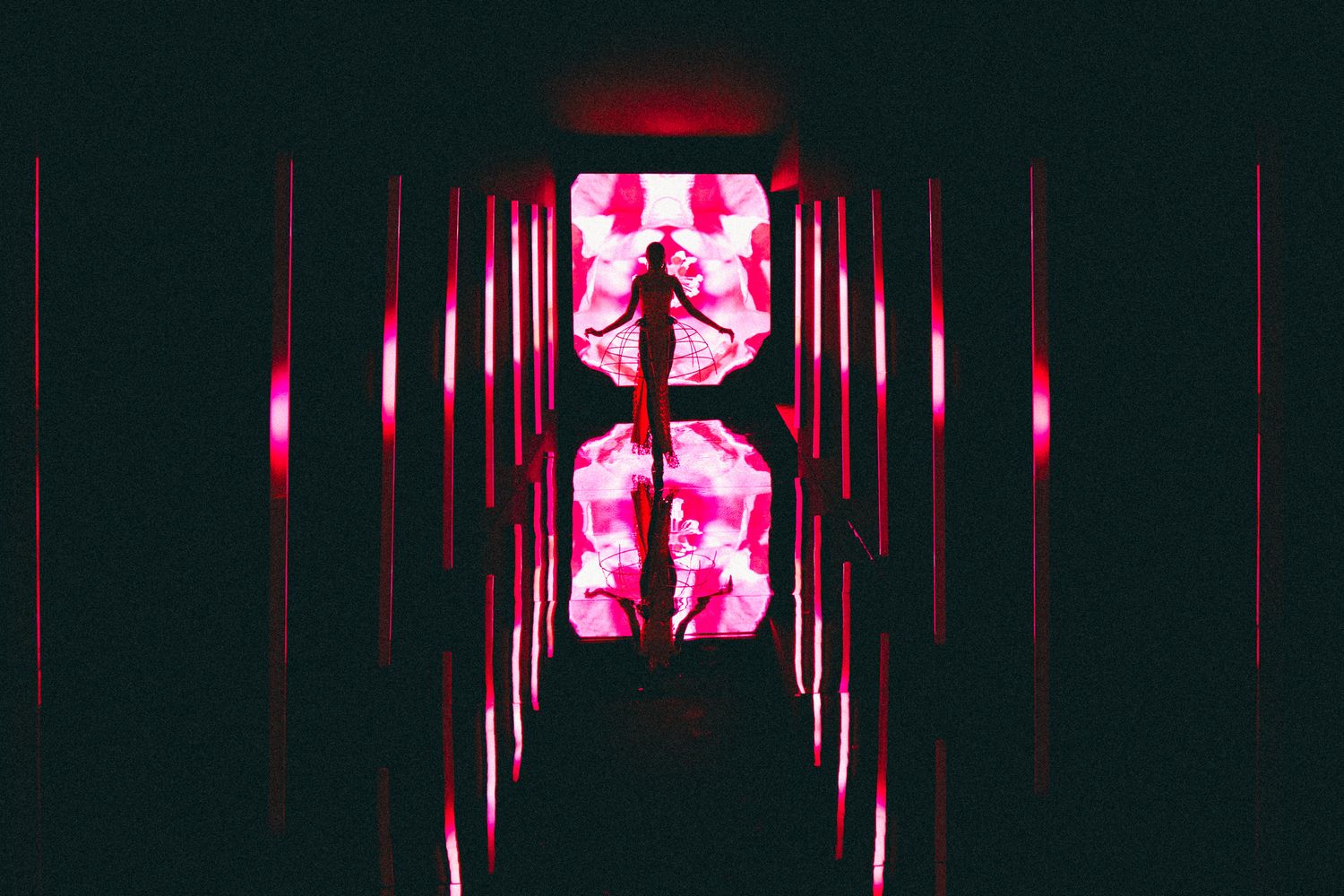 Silhouette of person in dark corridor with dramatic pink and red glowing light installation.