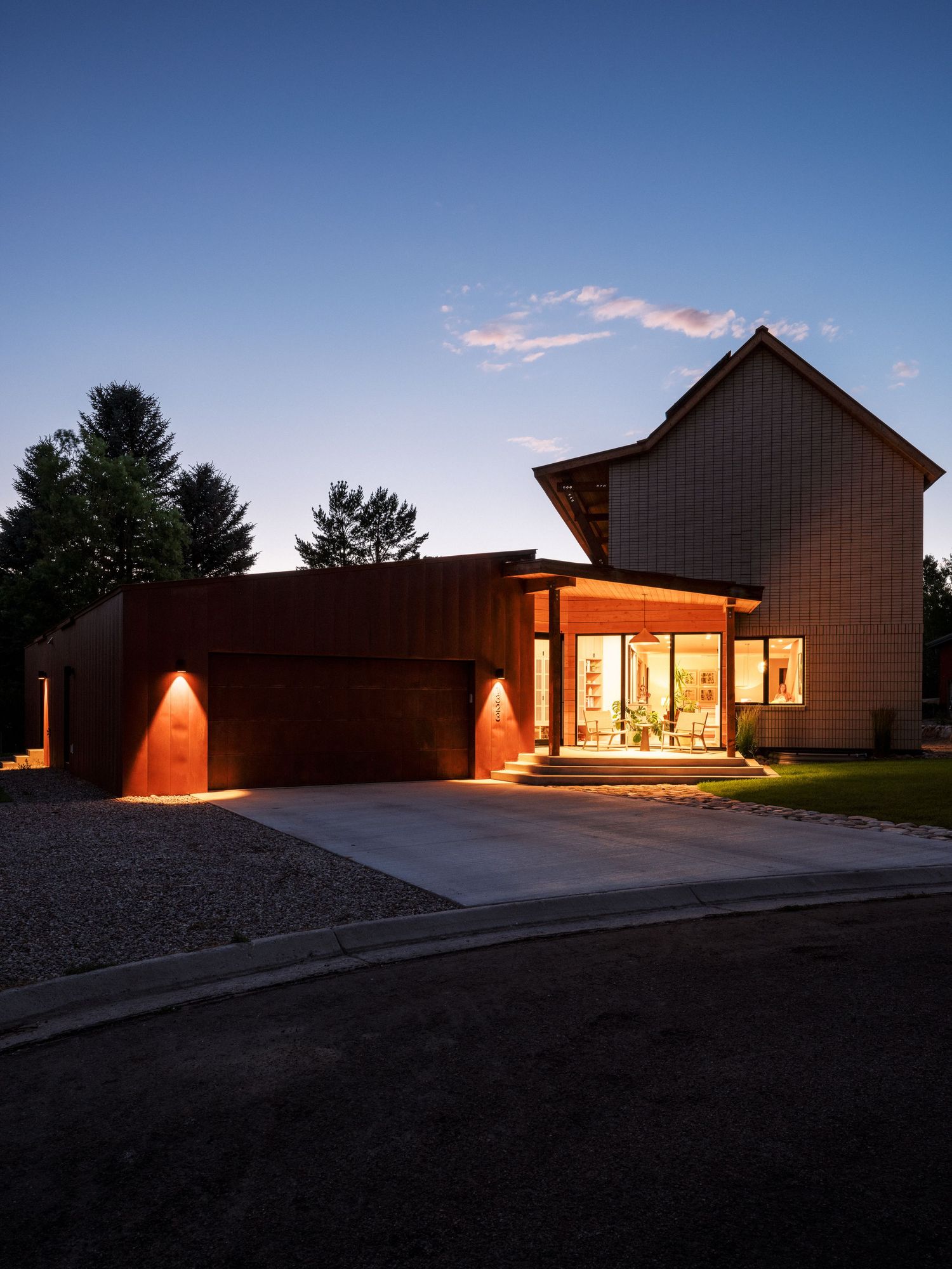 Modern house exterior at dusk with warm interior lighting glowing through windows.
