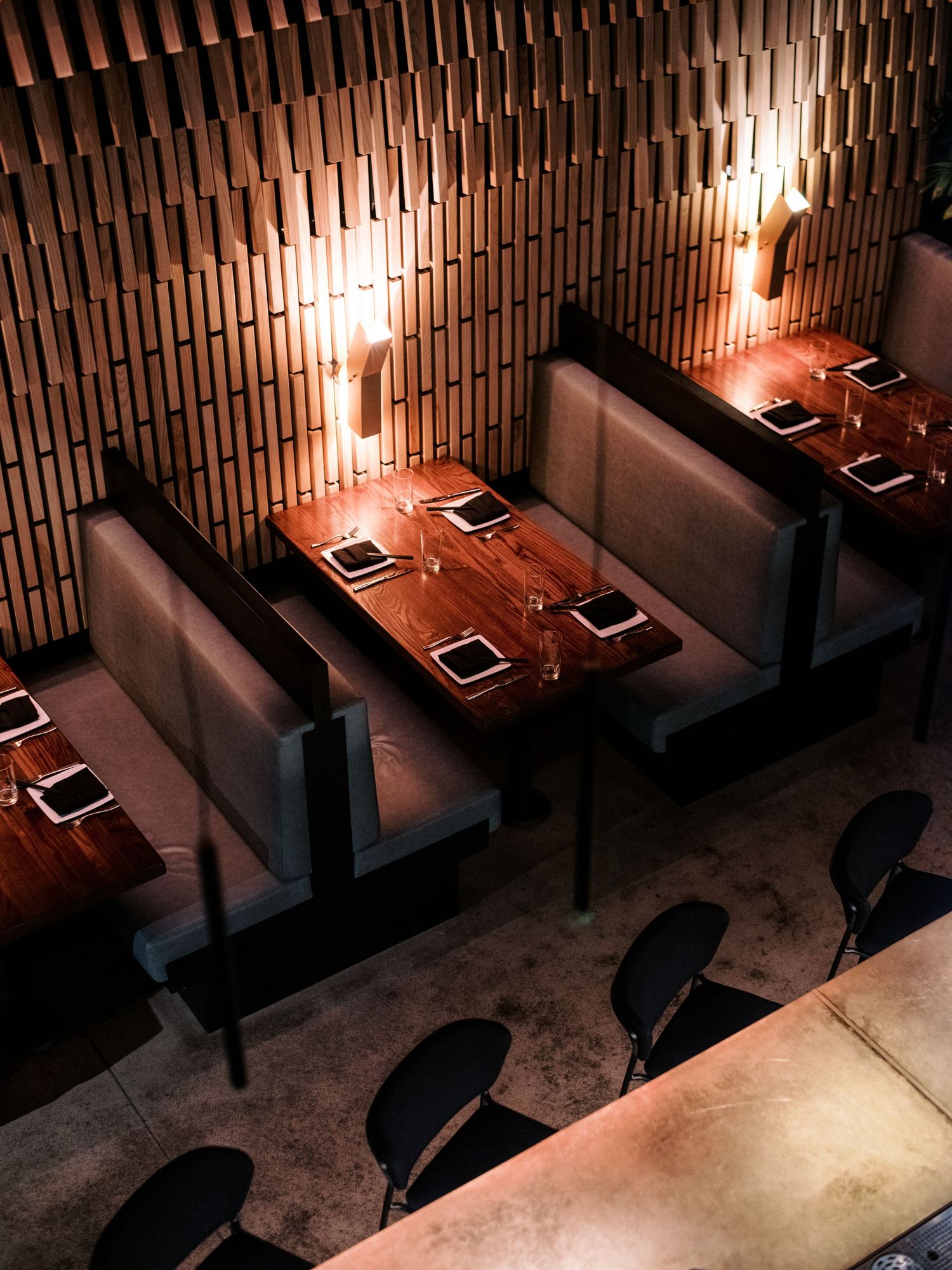 Upscale restaurant interior with wooden slat walls and intimate booth seating under warm lighting.