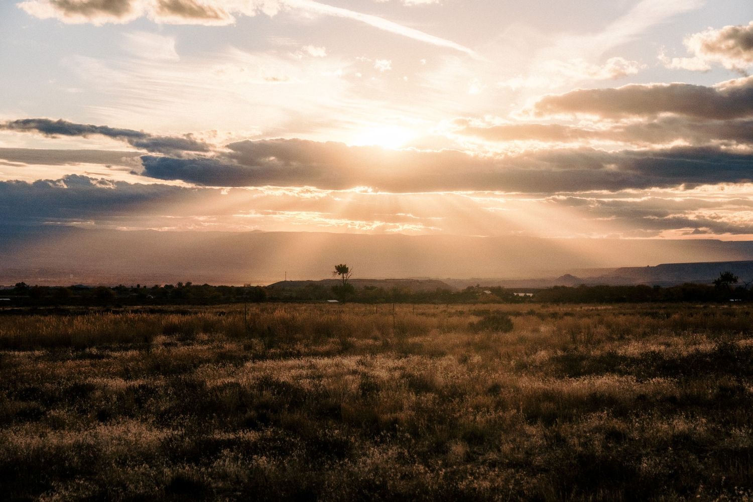 Dramatic sunset over desert plains with sunbeams breaking through cloudy sky.