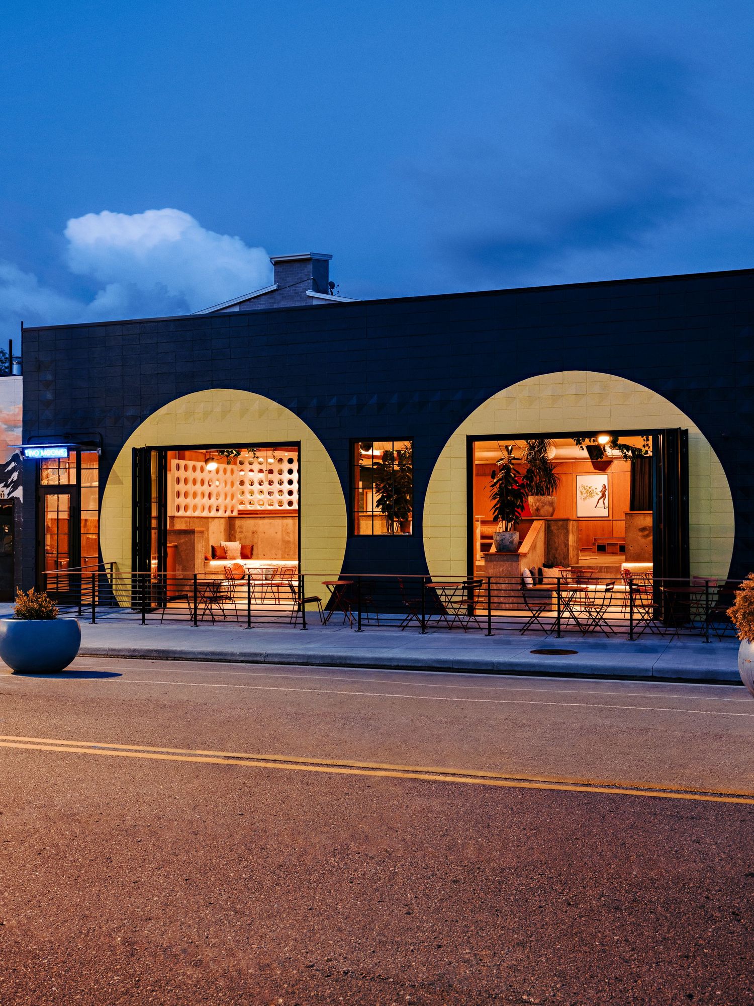 Contemporary retail building with curved architectural features and large windows lit up at twilight.
