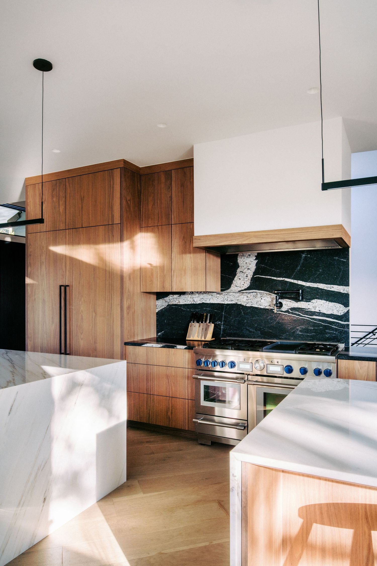Luxury kitchen with marble backsplash, stainless steel appliances and white waterfall countertop island.