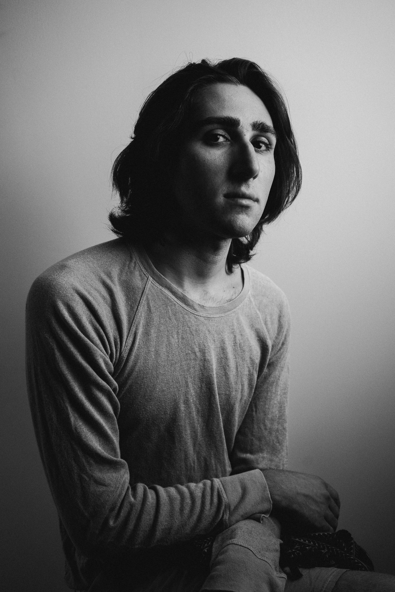 Moody black and white portrait of person in long-sleeved shirt against plain background.