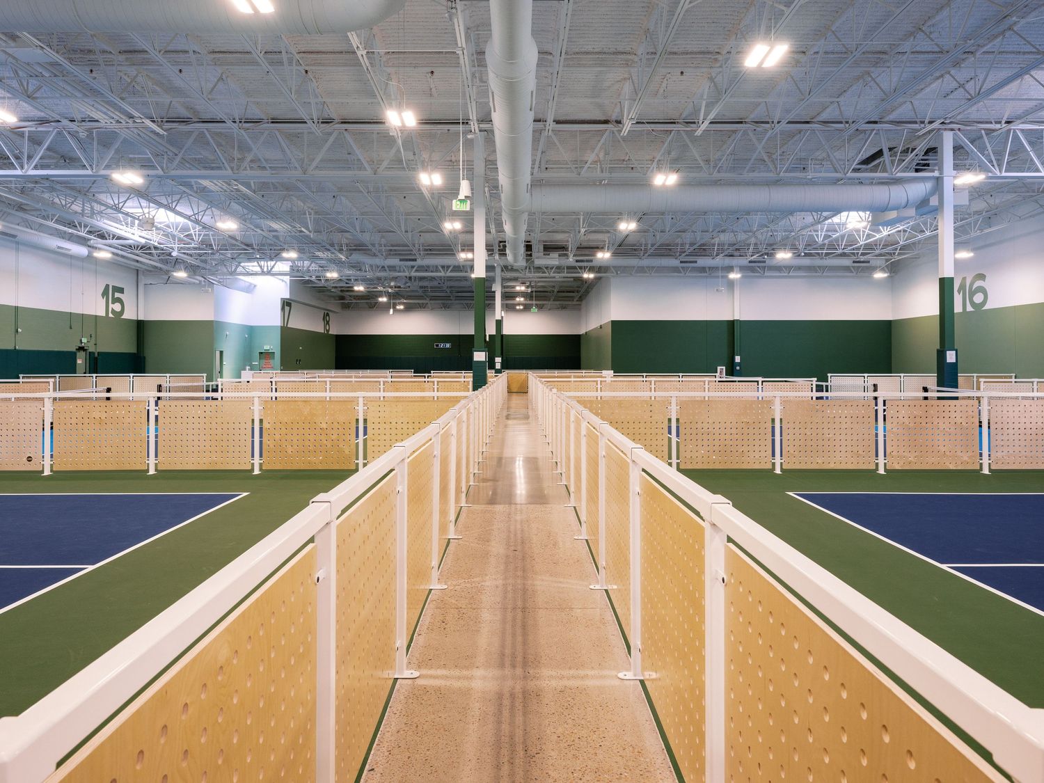 Long indoor sports facility with bright lighting and green turf flooring stretching into the distance.