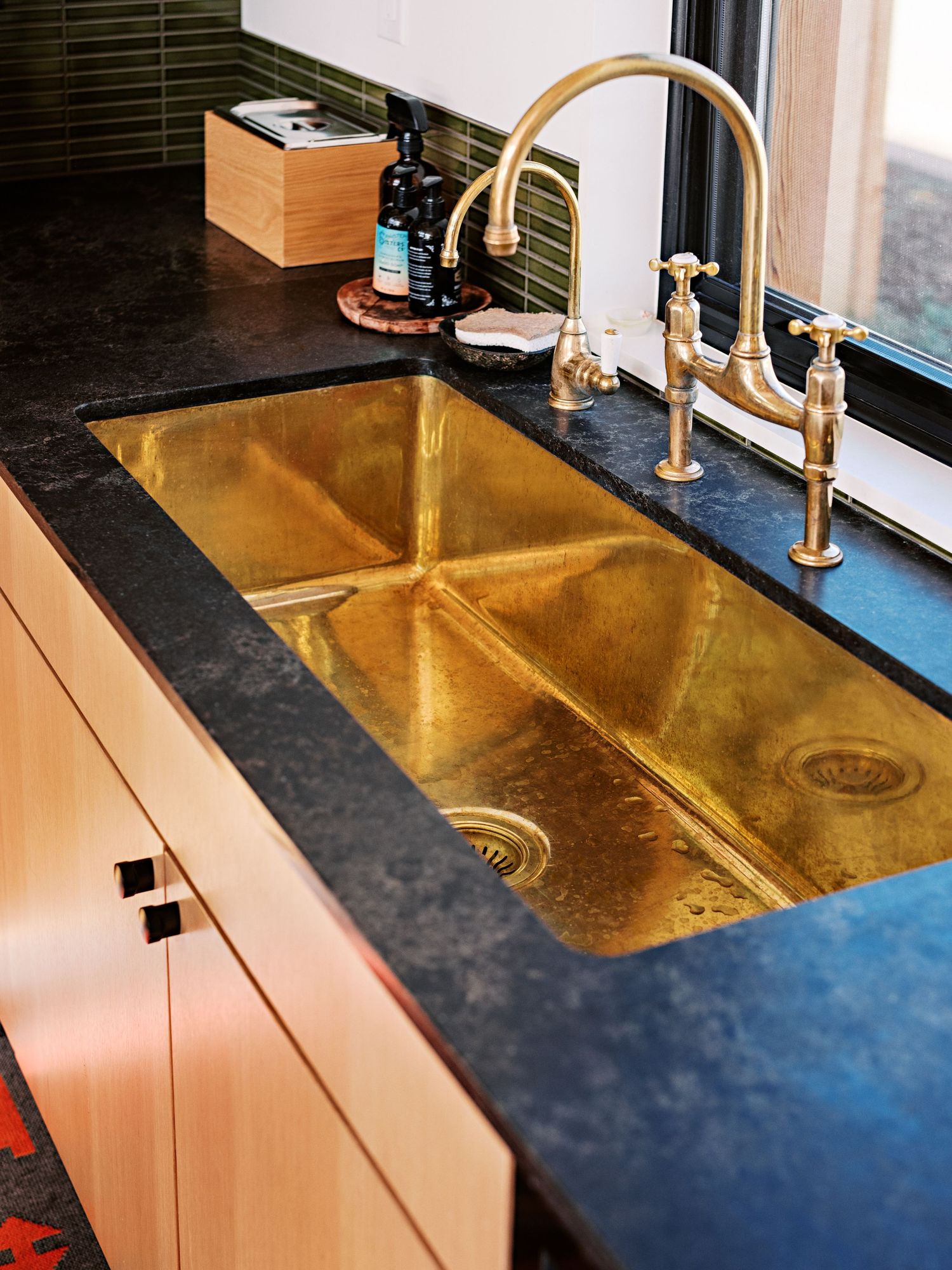 Luxury kitchen counter with brass faucet and gold-toned double sink against dark countertop.