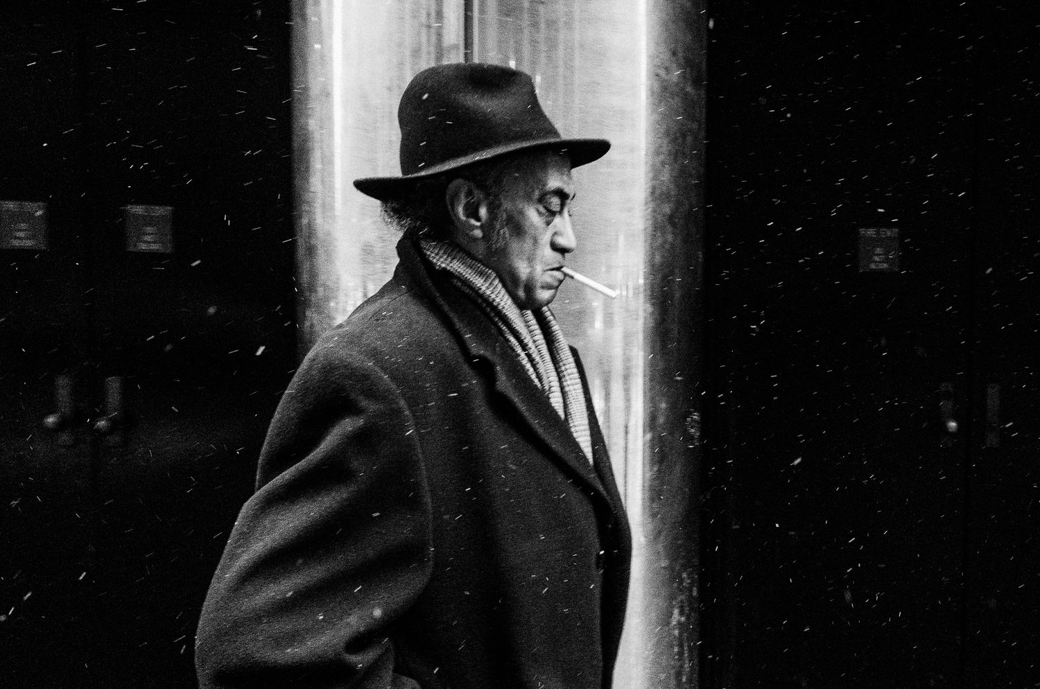 Silhouette of person in hat and coat walking past bright doorway.
