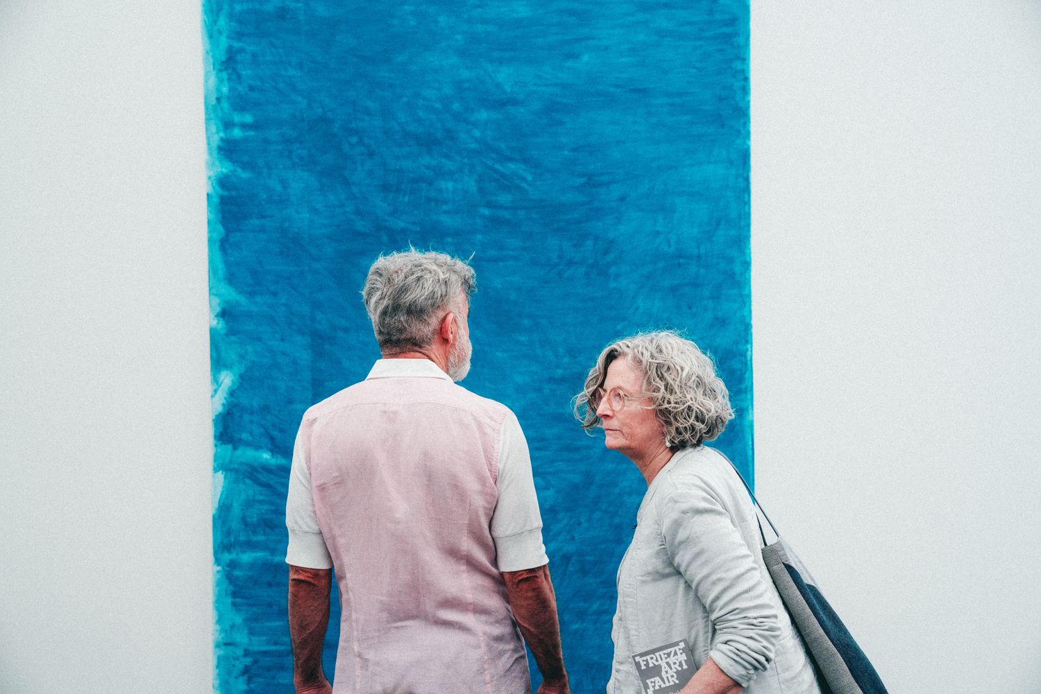 An older couple views a large blue abstract painting on a white gallery wall at a modern art museum.