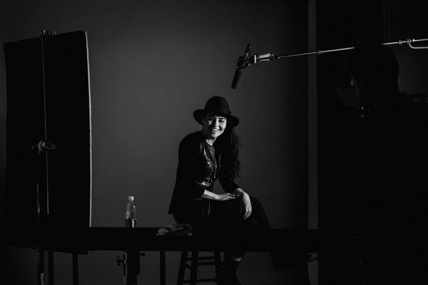 Silhouette of person in hat sitting on chair in studio with lighting equipment visible.
