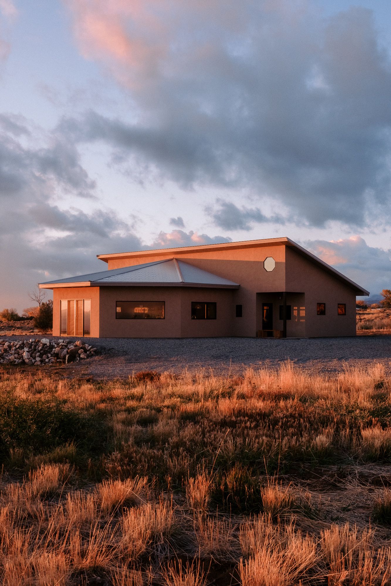 Modern industrial building with terracotta-colored walls illuminated by sunset light in a desert landscape.