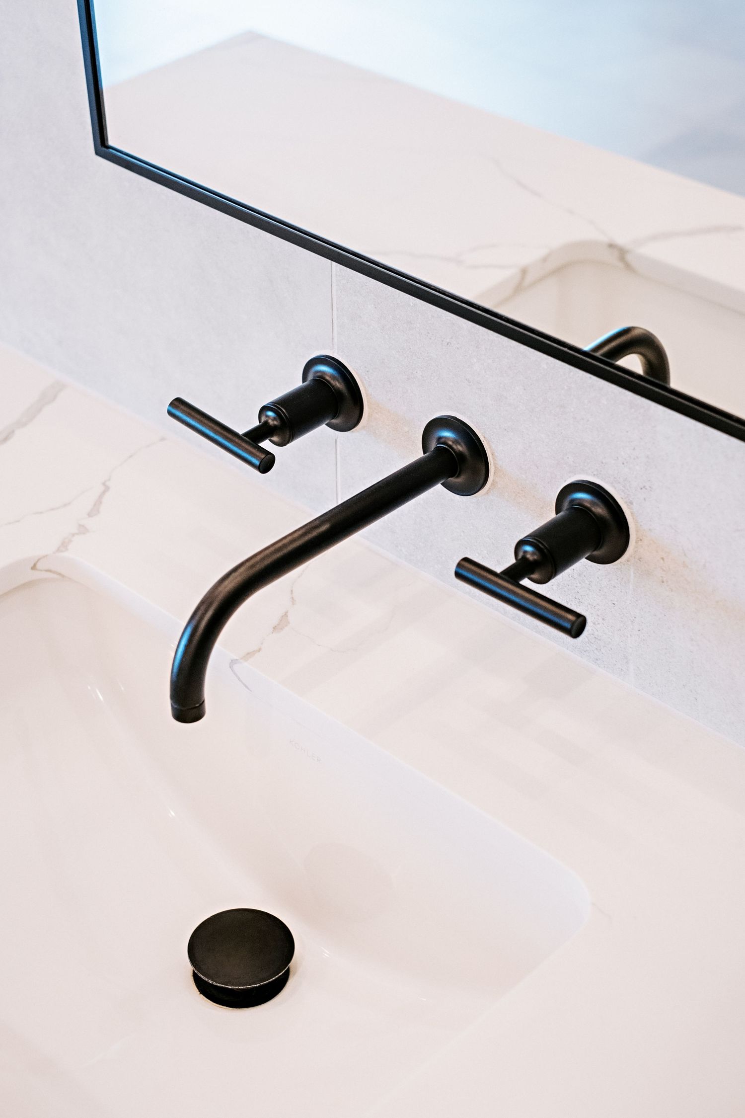 Minimalist black wall-mounted faucets against white tile in a modern bathroom design.