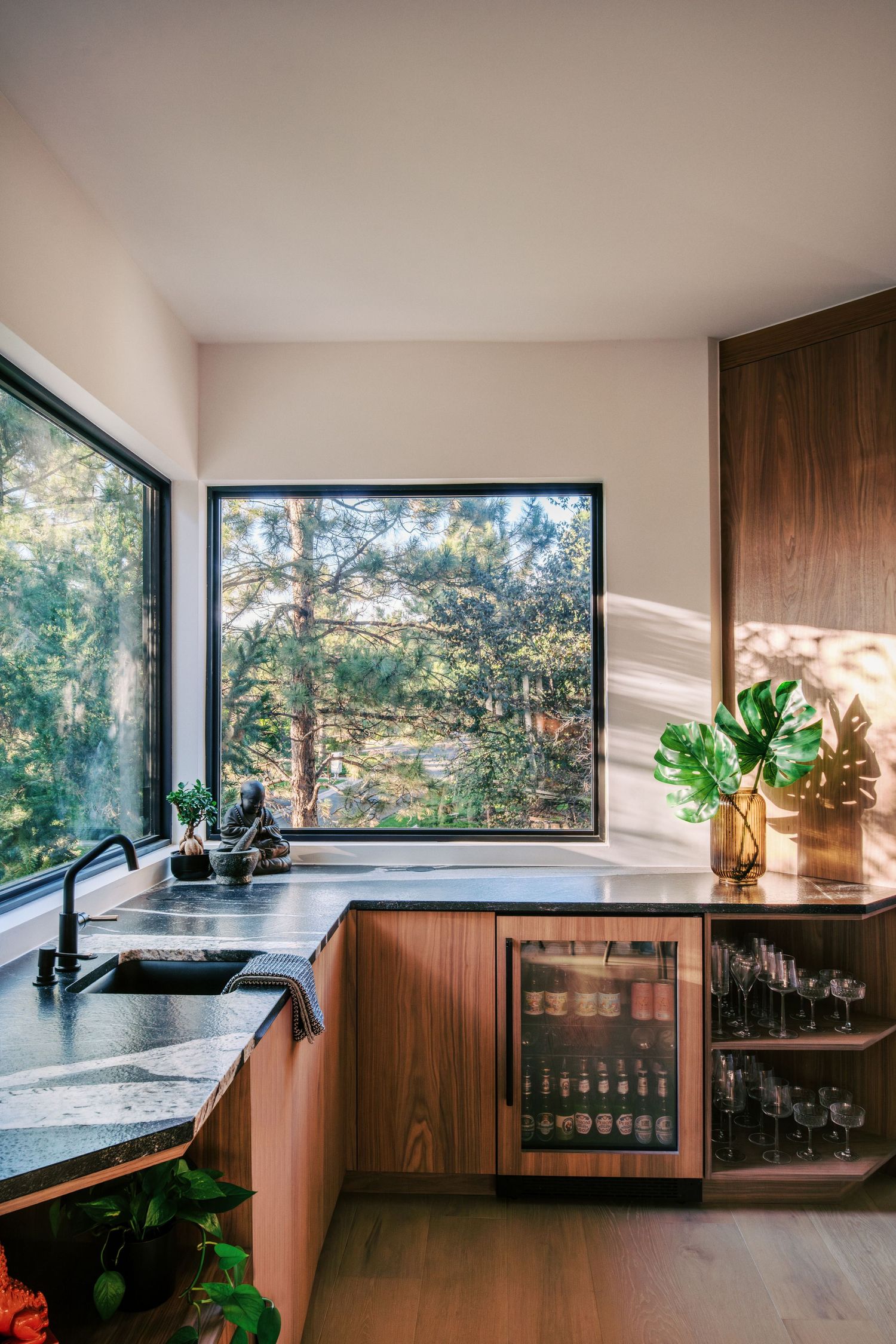 Modern kitchen with panoramic forest views features dark countertops and wooden cabinetry.