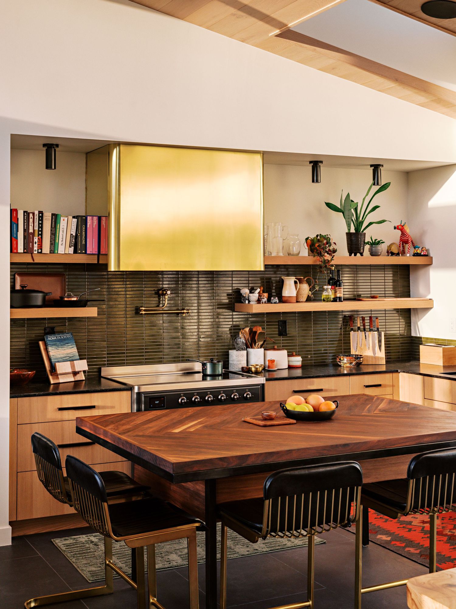 Modern kitchen dining area with wooden table, black chairs and floating shelves against a grey backsplash.
