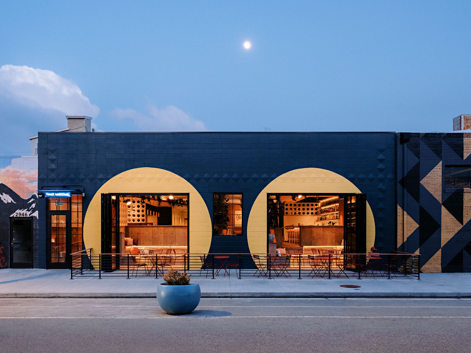 Modern storefront with arched windows and outdoor seating at dusk.