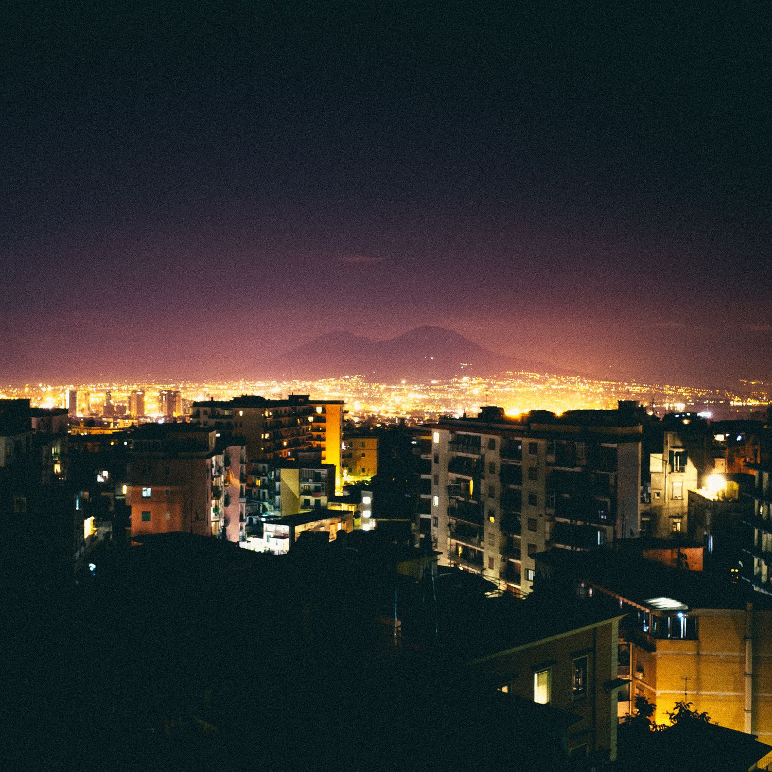 Panoramic cityscape at night showing illuminated buildings and streets stretching across the horizon.