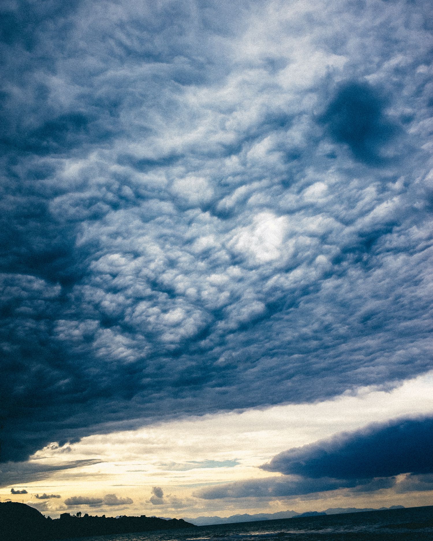 Dramatic time-lapse sequence of dark storm clouds rolling across a moody sky at sunset with golden light on horizon.