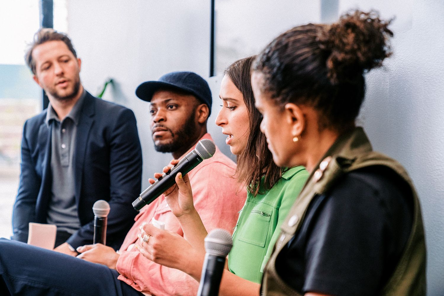 Four diverse panelists seated in a row during a professional discussion event, one holding a microphone.