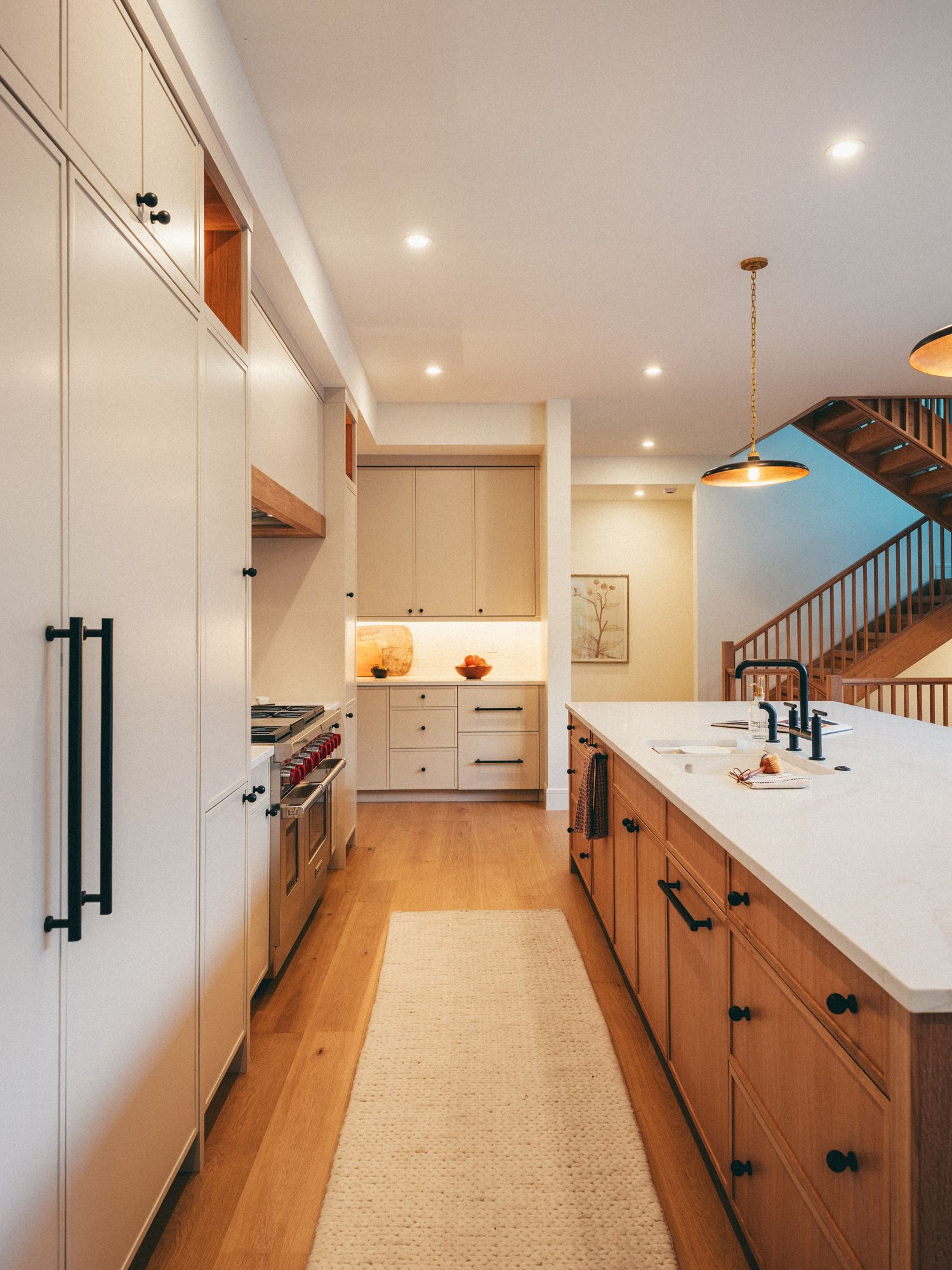 Modern kitchen with white upper cabinets, warm wood lower cabinets, white quartz island, pendant lights, and hardwood floors.