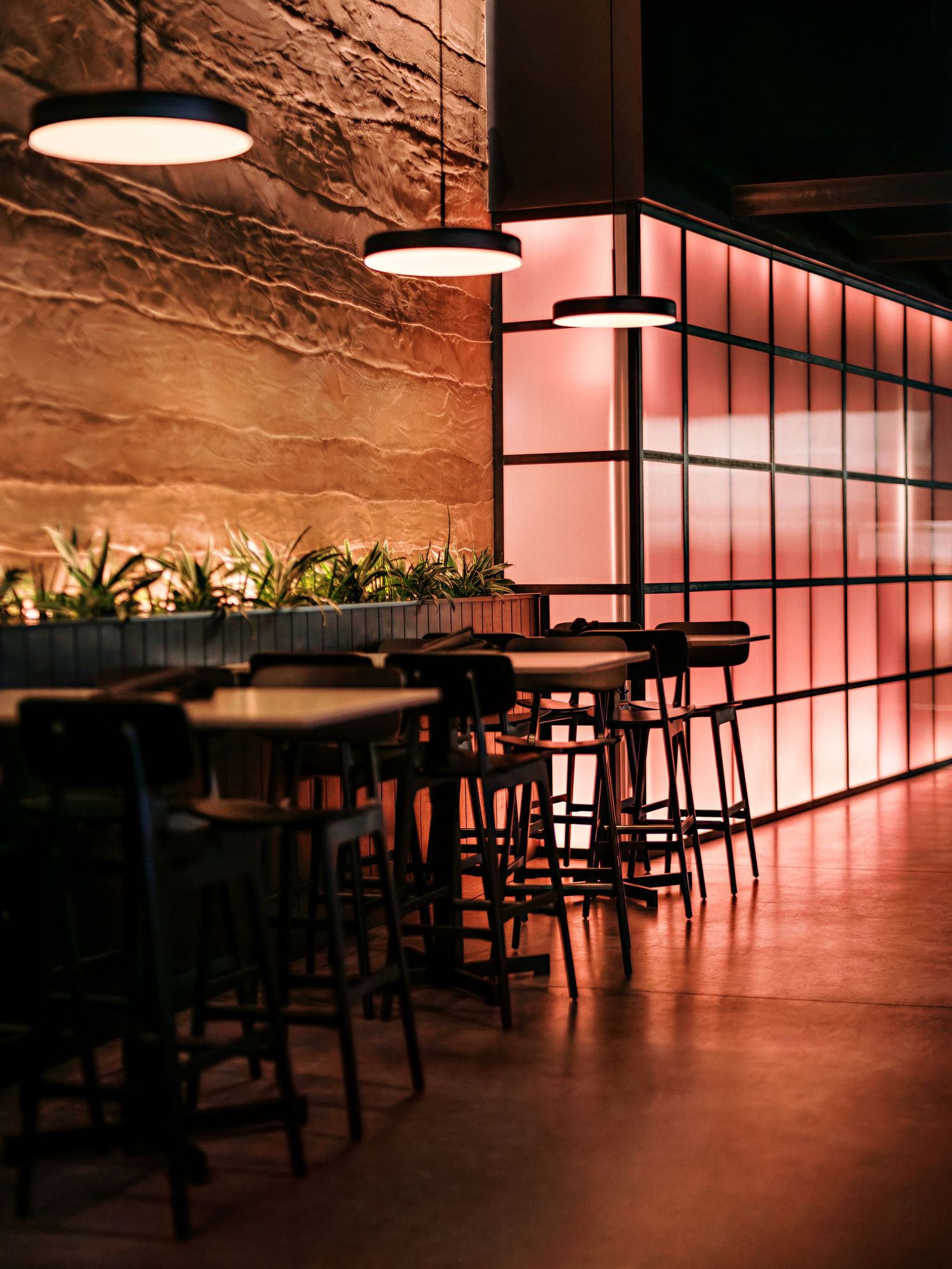 Minimalist restaurant space with pink ambient lighting and industrial-style ceiling fixtures.