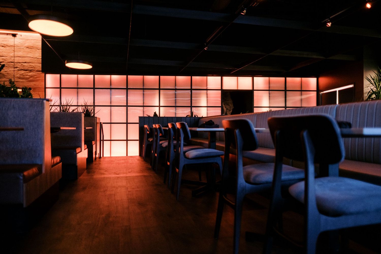 Dimly lit restaurant interior with pink backlit wall panels and comfortable booth seating.
