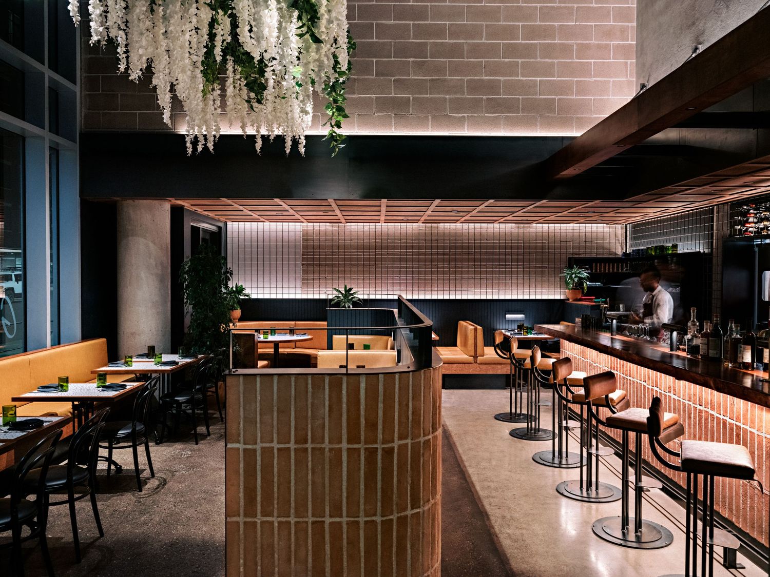 Elegant dining space with curved bar counter, hanging plants, and leather bar stools.