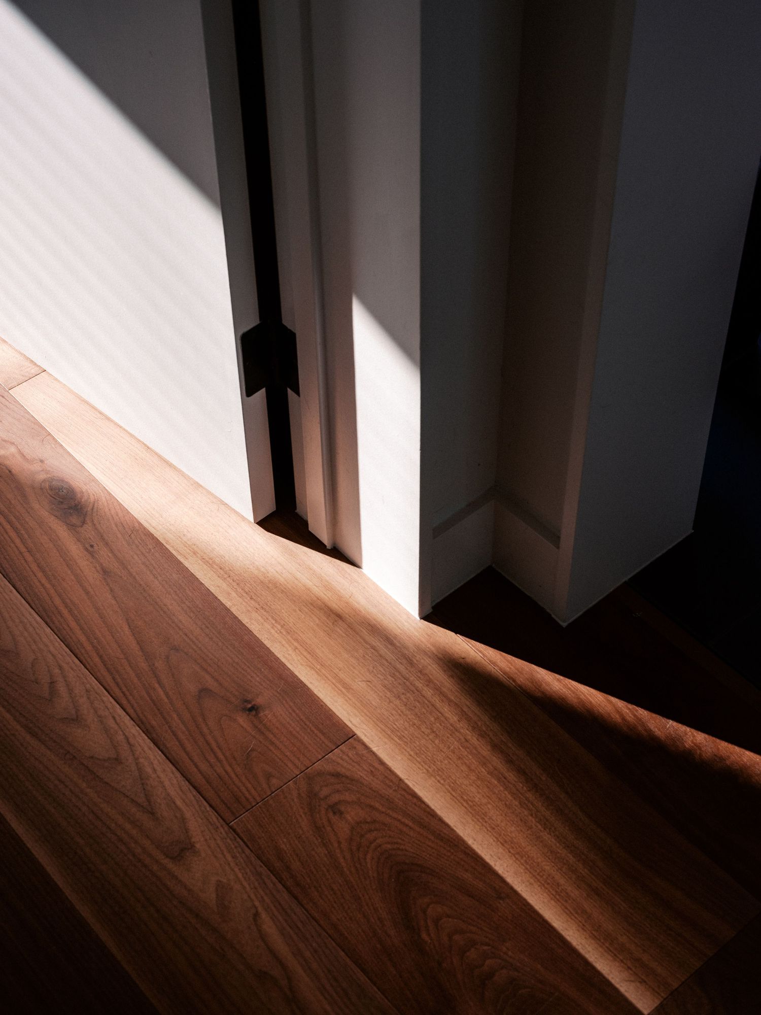 Sunlight casting dramatic diagonal shadows across wooden flooring in an interior space.