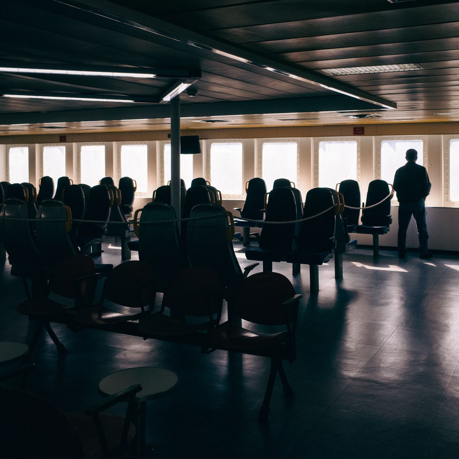 Silhouette of a person standing in a dimly lit ferry cabin with rows of empty passenger seats.
