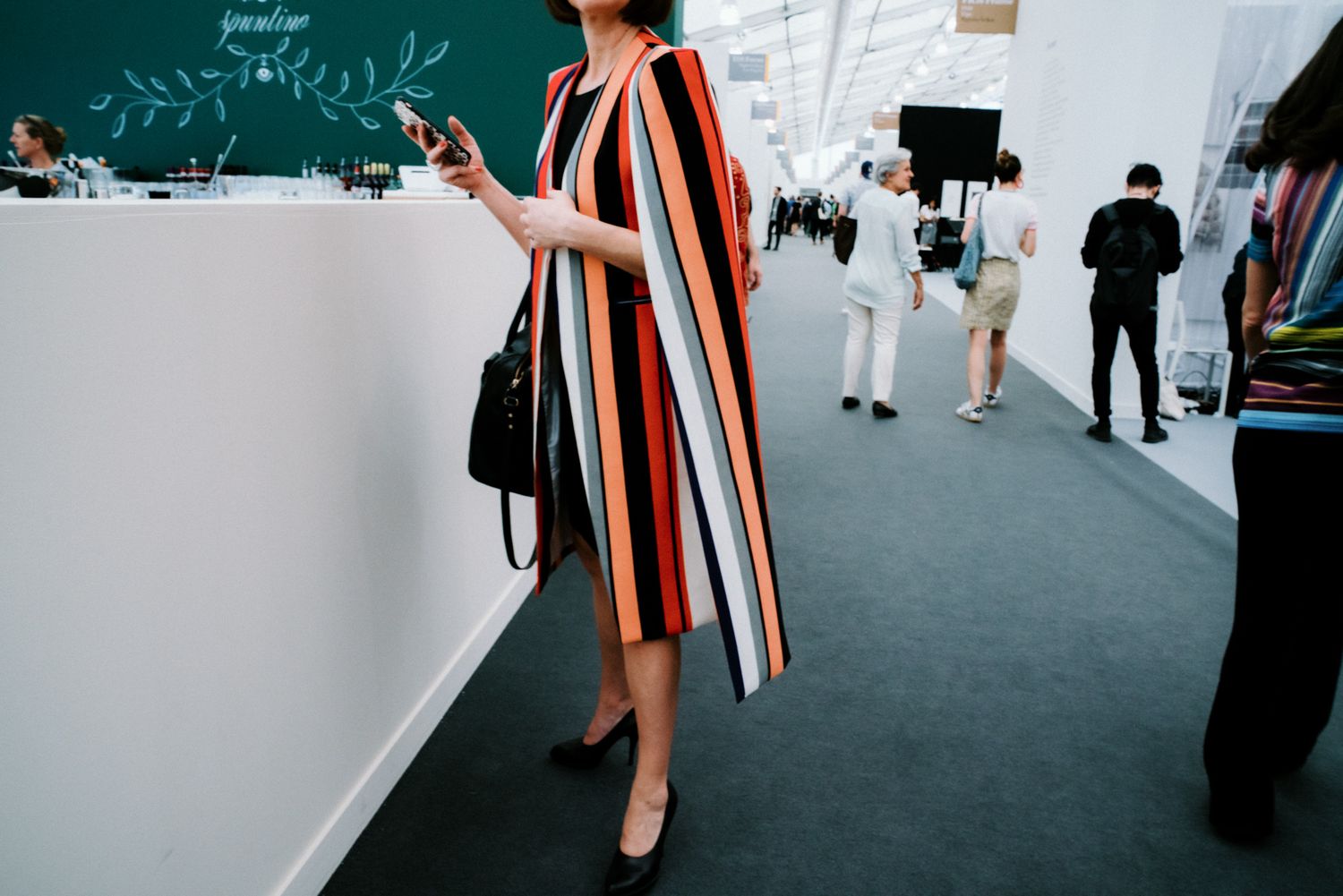 Woman in bold striped multicolor dress holding phone at modern event venue.