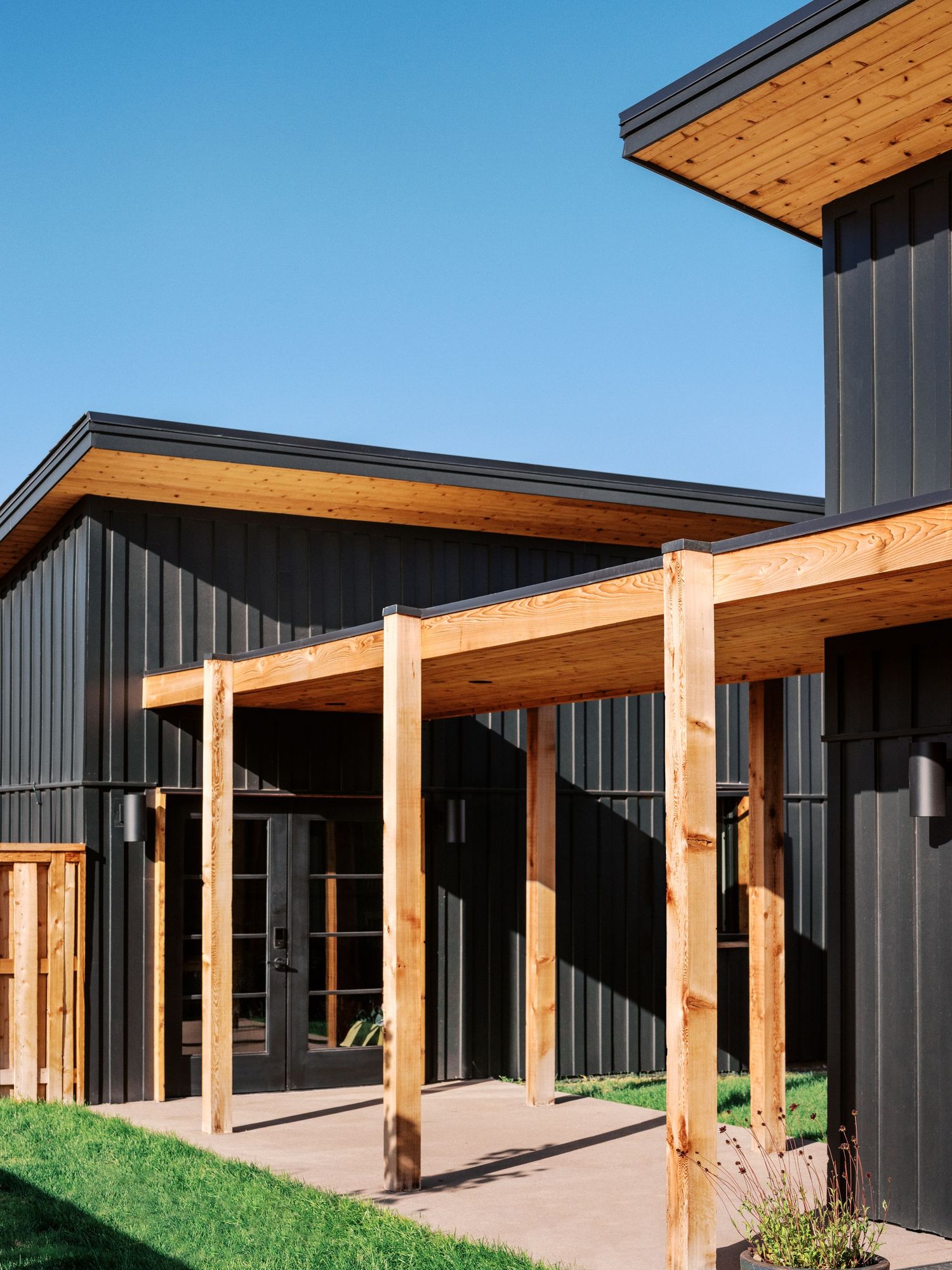 Covered walkway with exposed wooden beams and posts along modern black building exterior.