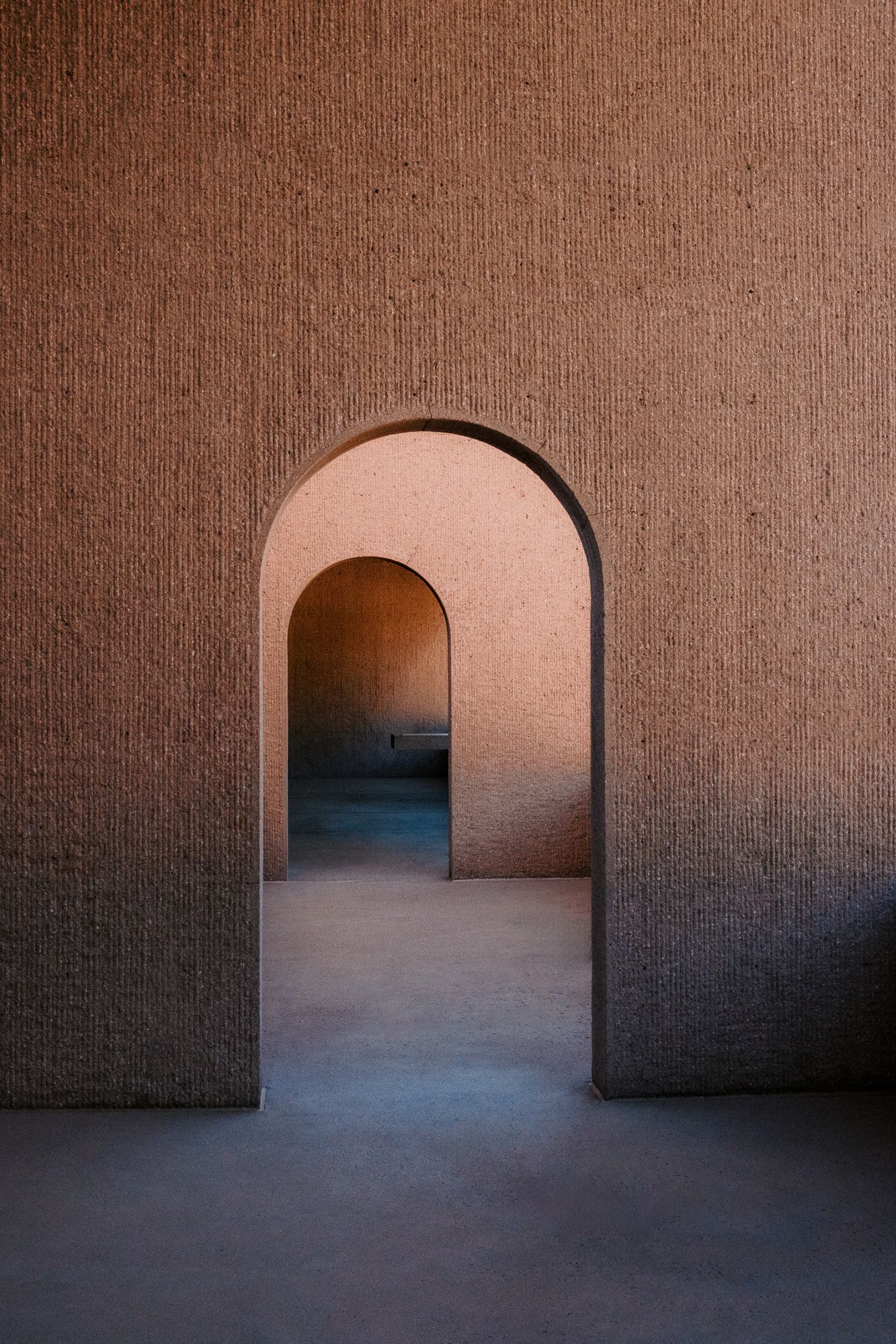 Minimalist architectural space with repeating terracotta arches creating a curved hallway.