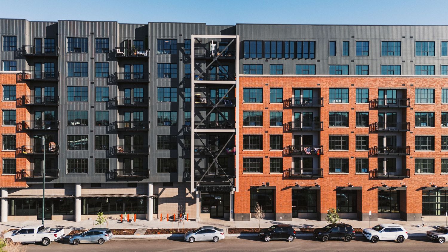 Urban panorama of modern apartment buildings with glass facades and parked cars along the street.