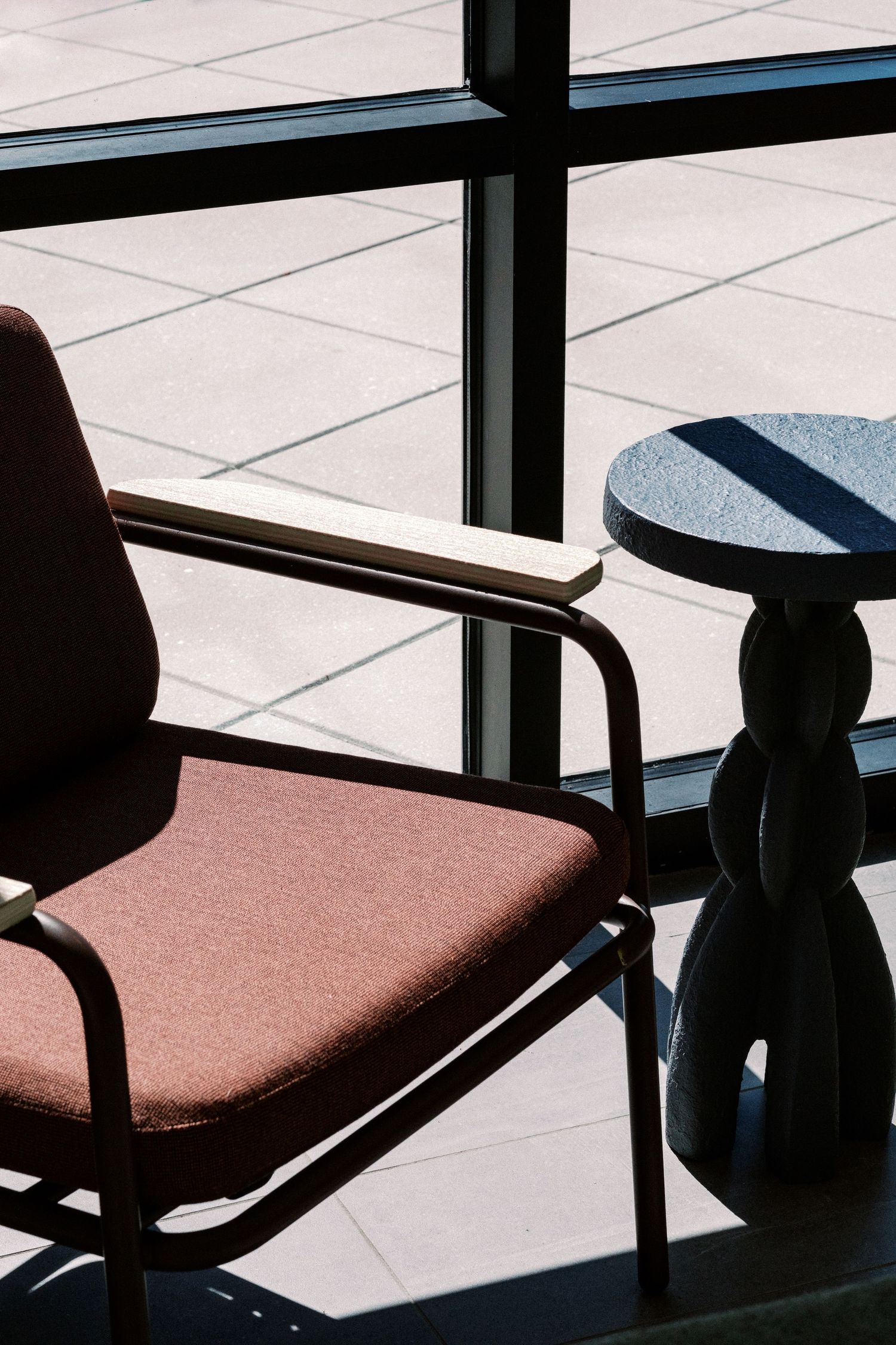 Modern brown upholstered chair with armrests next to decorative side table in sunlit room.