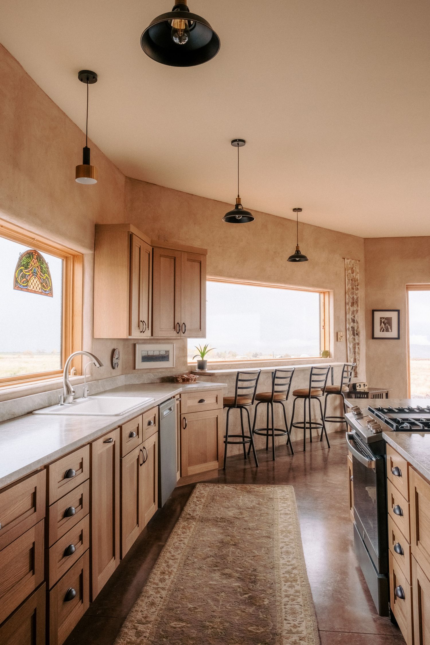 Modern kitchen with wooden cabinets, pendant lights, and large windows overlooking a scenic view.