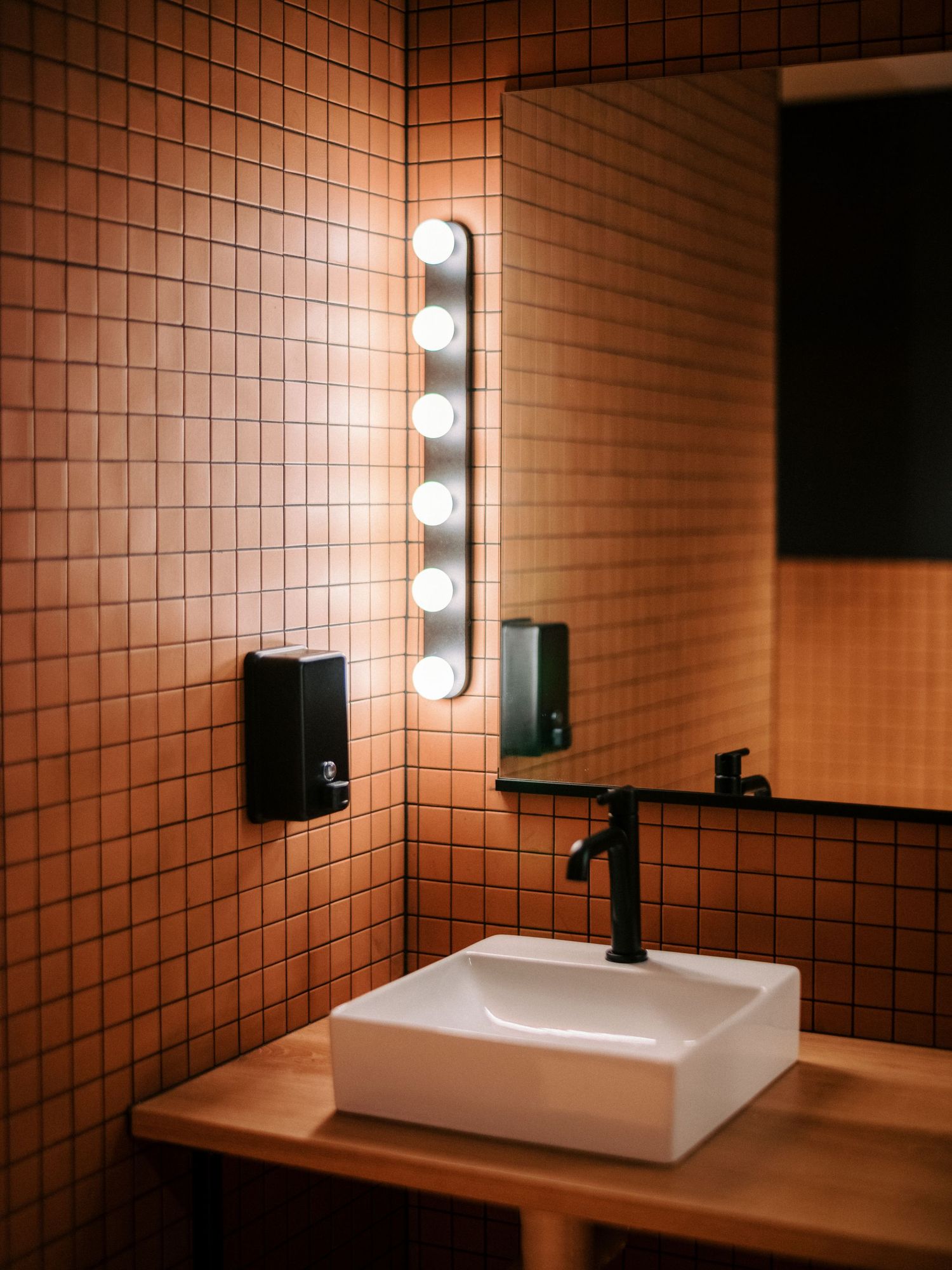 Contemporary bathroom vanity with square tile walls and modern vessel sink under vertical lighting.