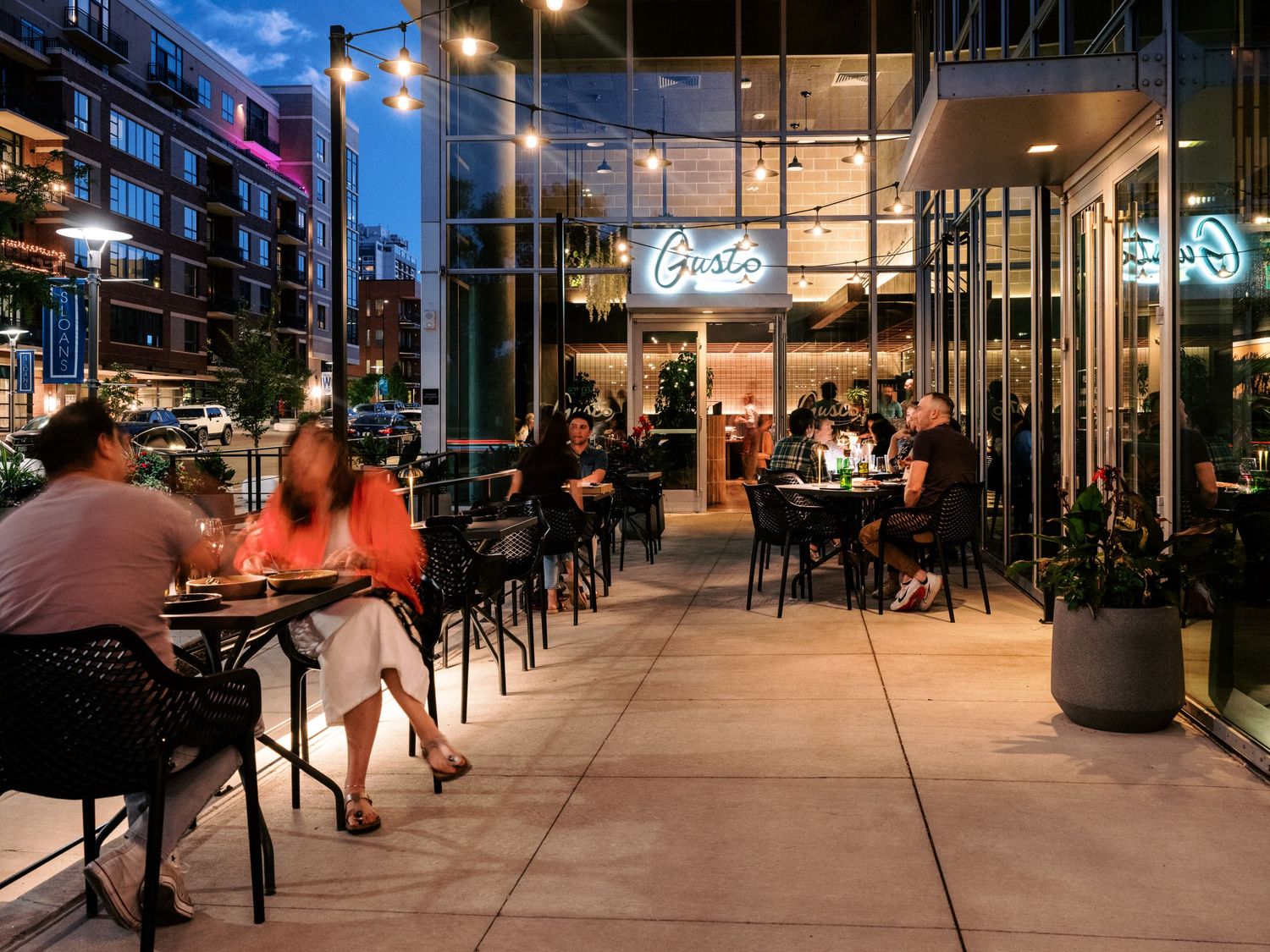 Restaurant patio dining area with outdoor seating and neon signage at dusk.