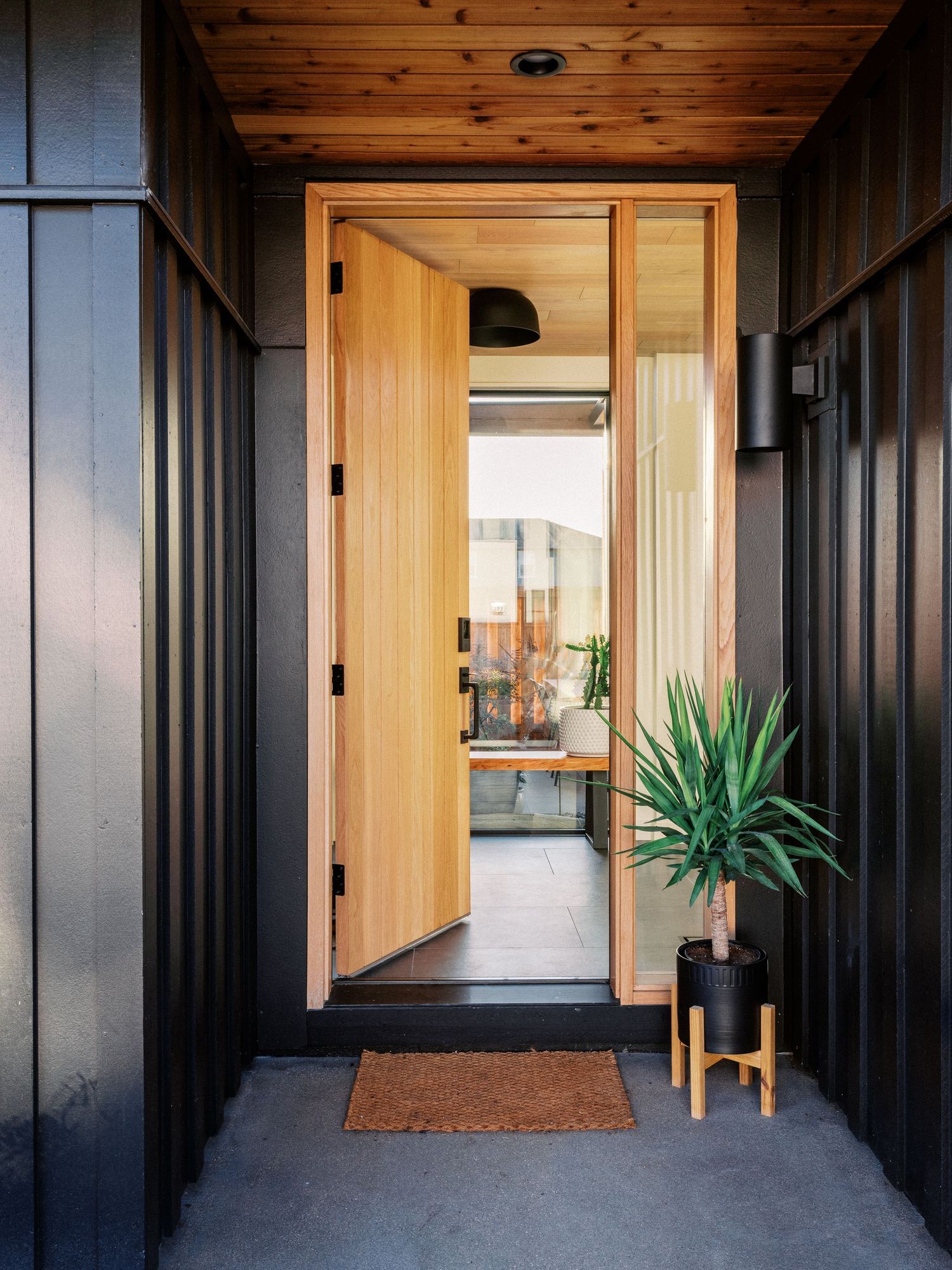 Modern entryway with black vertical siding and wooden door framed by minimalist architecture.