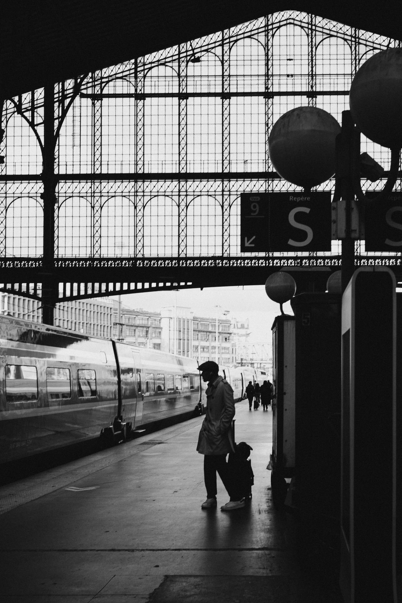 Black and white photograph of a train station platform with arched glass ceiling and silhouetted figures.