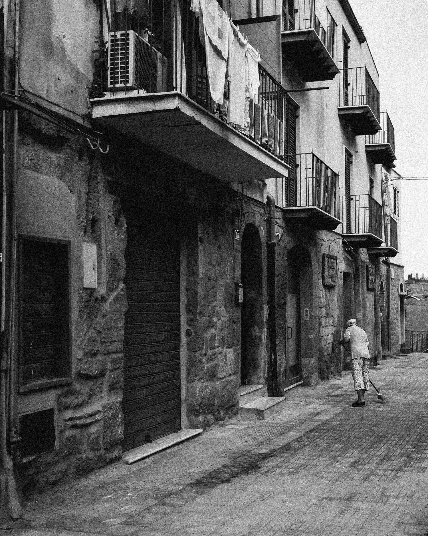 Black and white photos of narrow cobblestone streets with old buildings and balconies in a Mediterranean town.