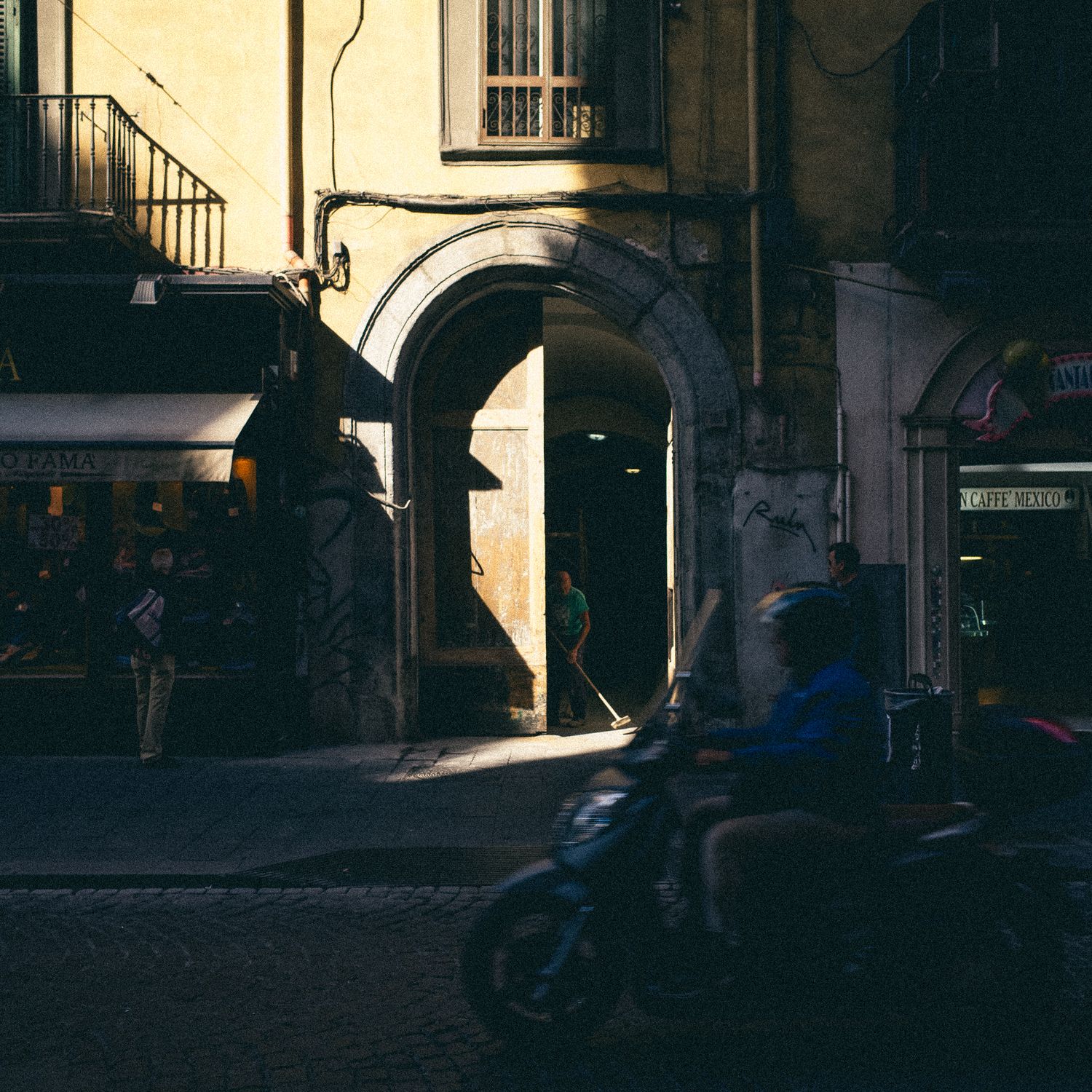Sunlight creates dramatic shadows and contrast on a historic building facade with arched windows and doorways.